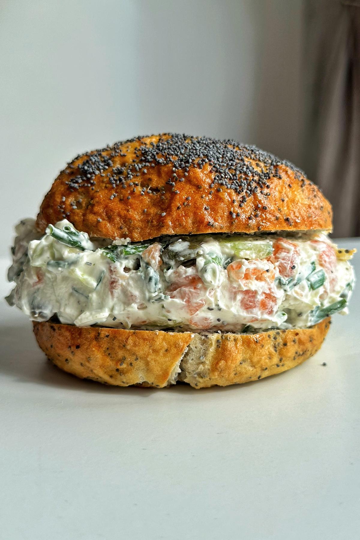 Side portrait of a poppy seed bagel stuffed with a salmon cream cheese filling.