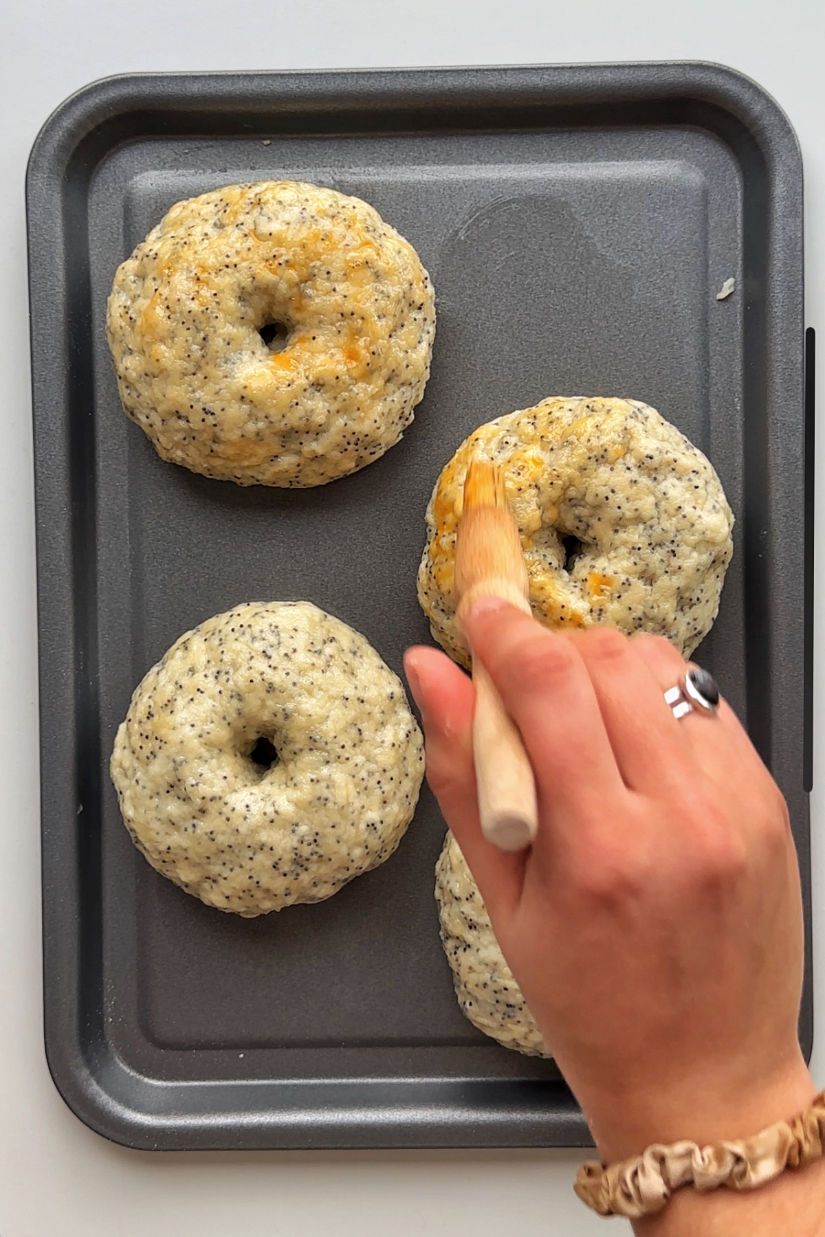 Brushing egg over boiled bagels on a baking tray.