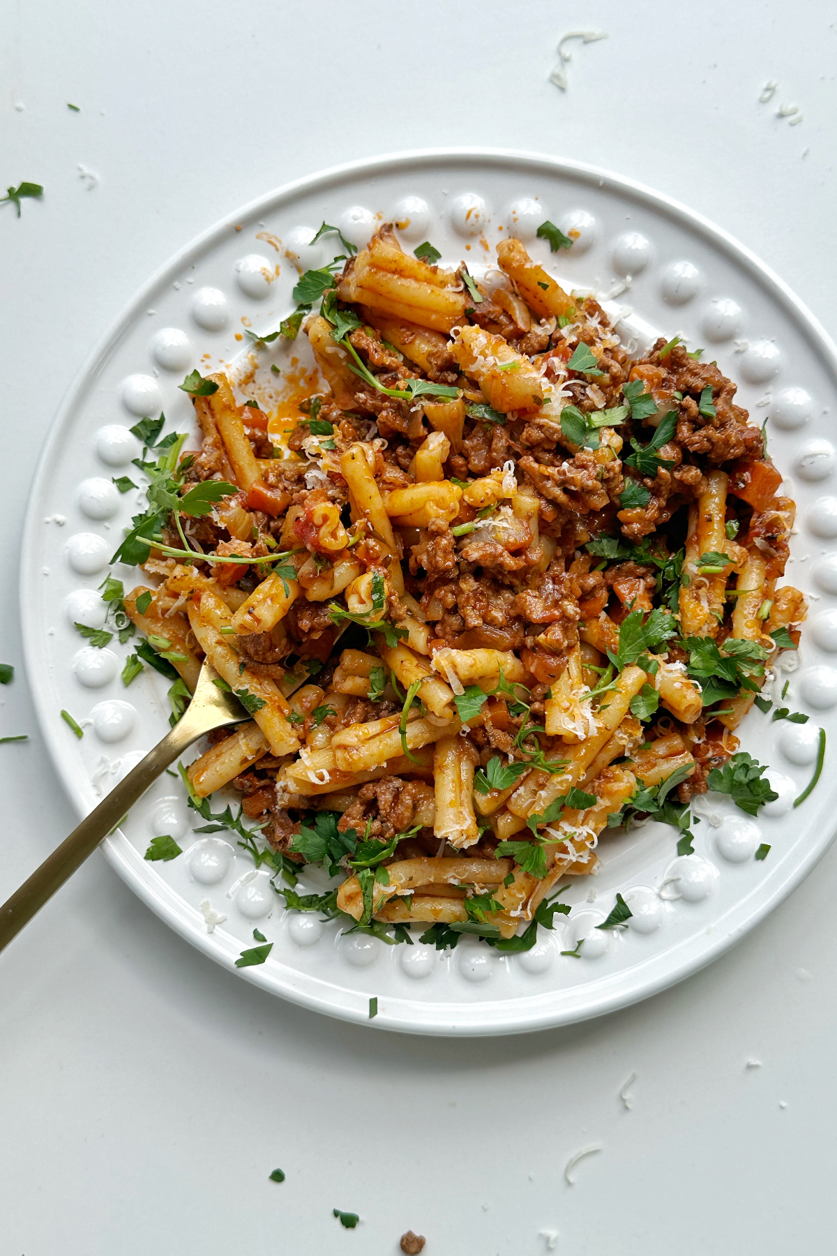 A bowl of casarecce bolognese with a fork in a white bowl.