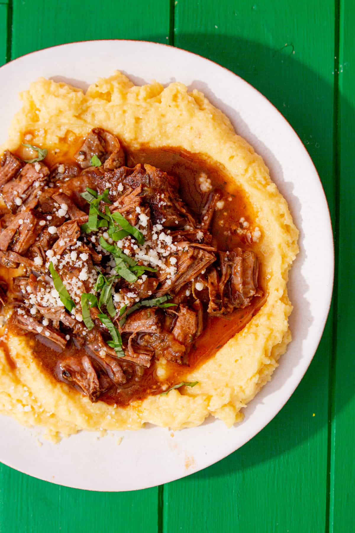 Tender braising steak over mashed potatoes on a green background.
