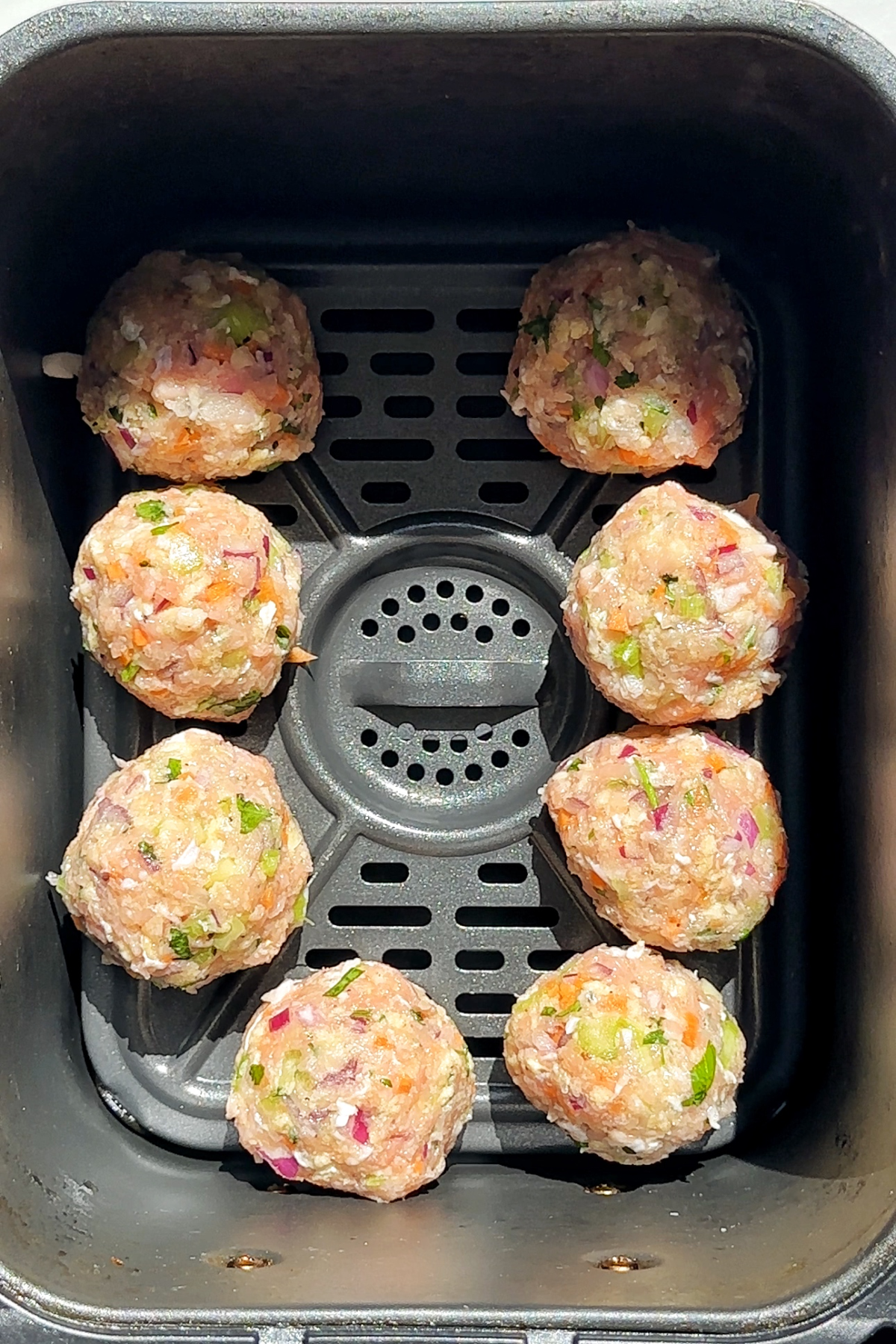 Chicken meatballs placed in side of an air fryer.