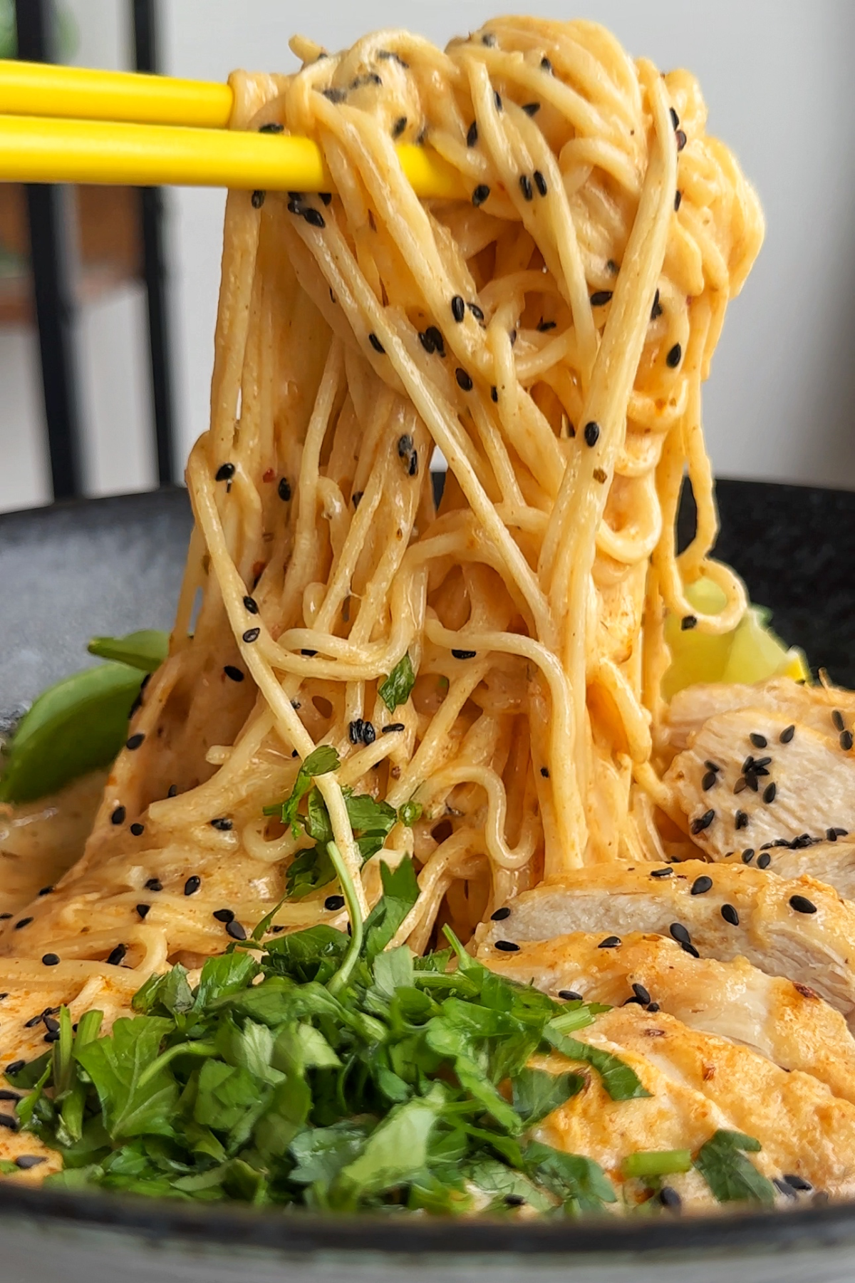 Noodle pull from a black bowl of lemon chicken ramen. 
