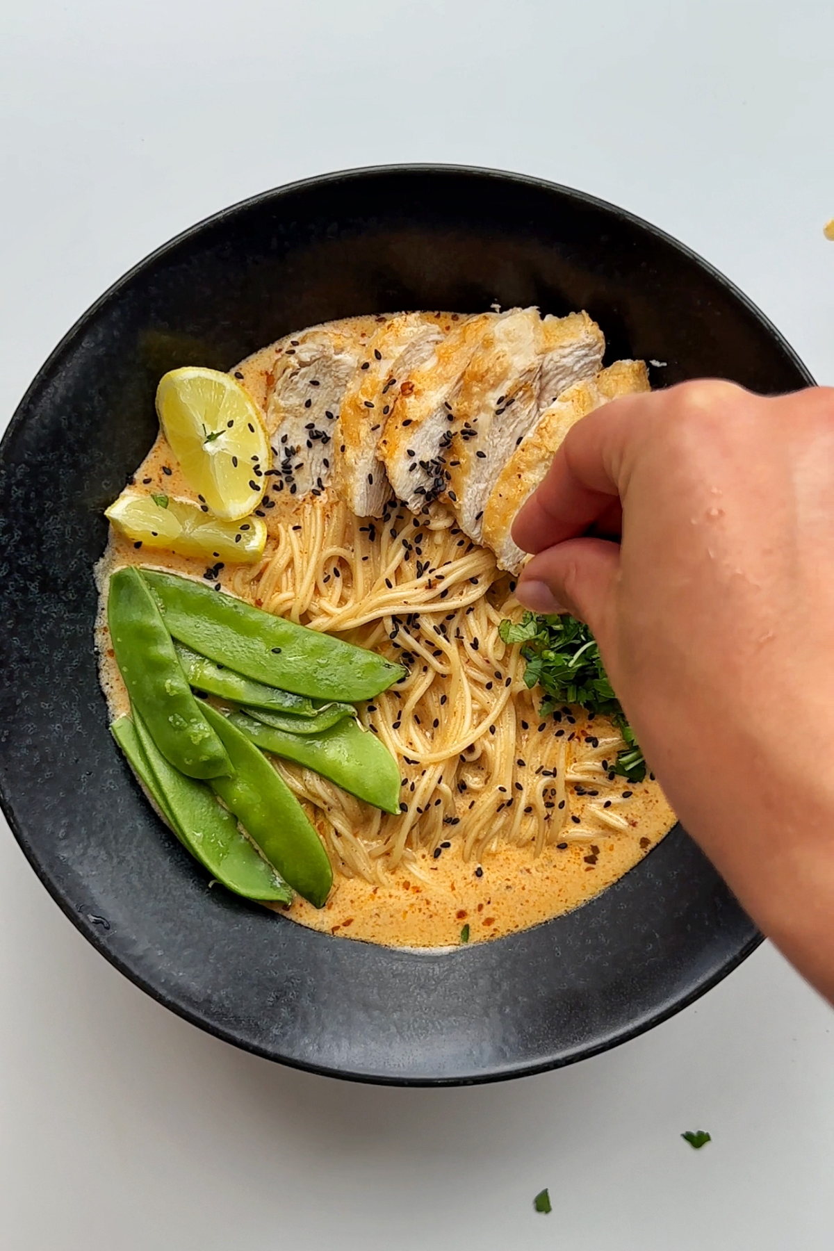 Adding parsley onto a bowl of lemon chicken ramen. 