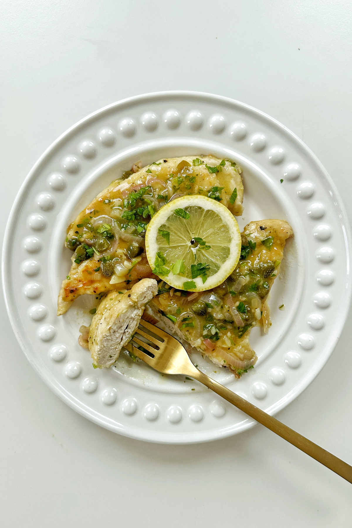 Picking up a sliced bit of chicken piccata with a golden fork.