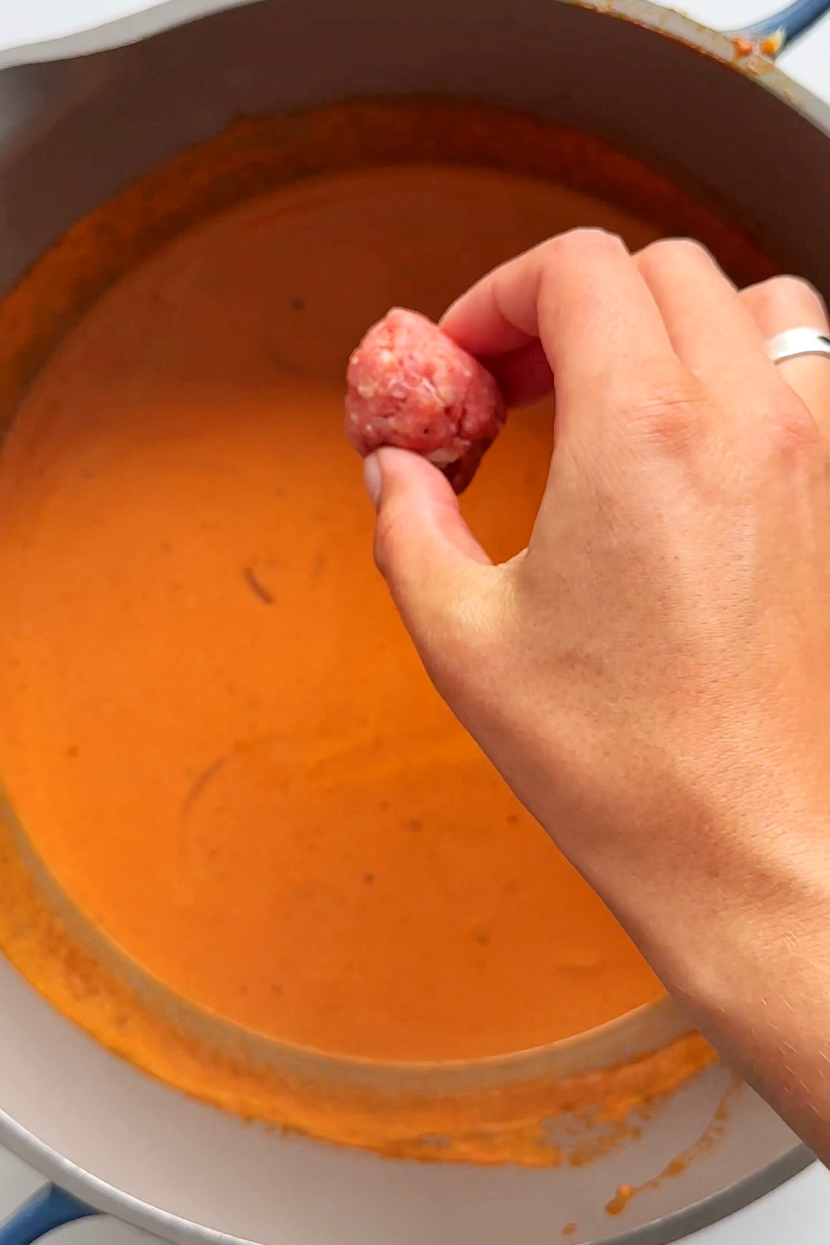 Dropping little meatballs into tomato soup.