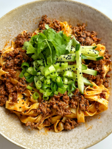 Close up of egg noodles with ground beef topped with cucumber, cilantro, and green onions.