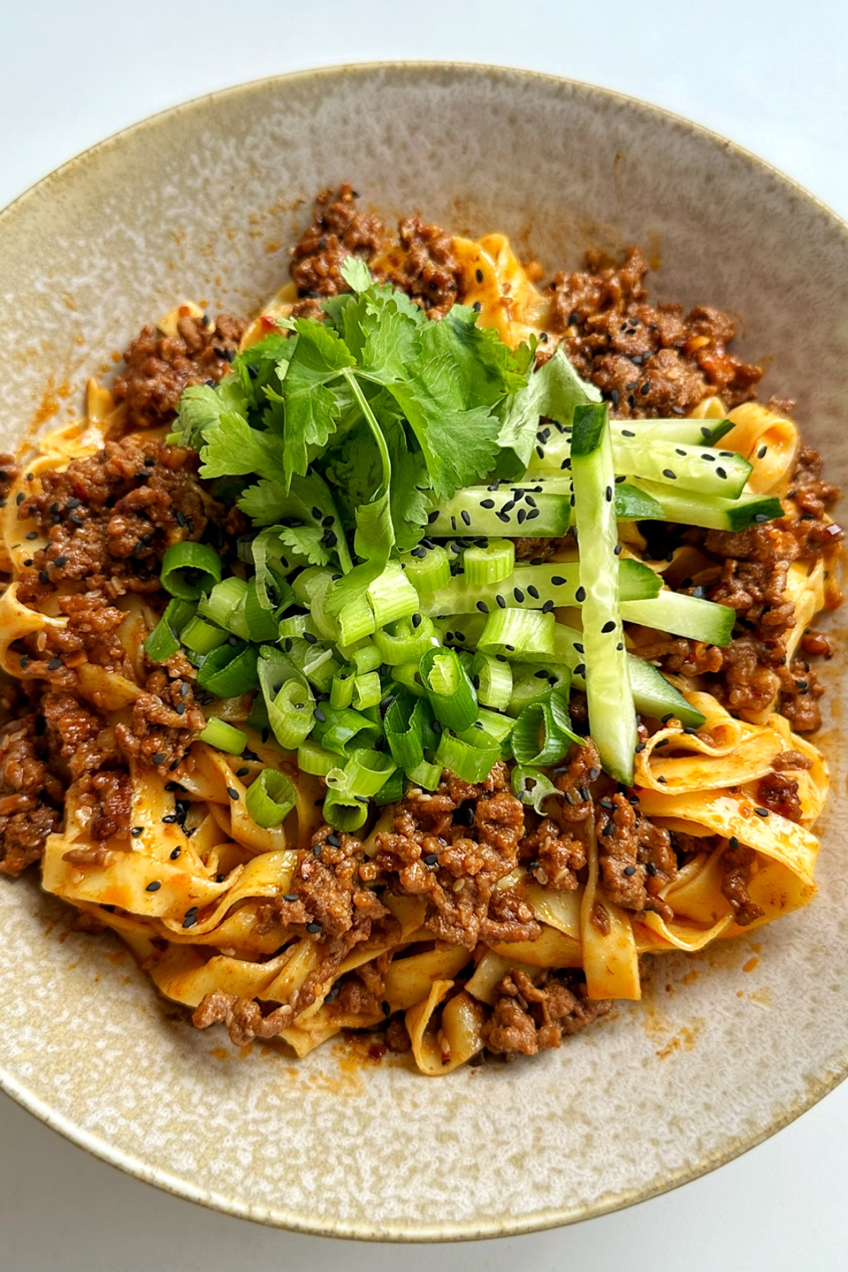 Close up of egg noodles with ground beef topped with cucumber, cilantro, and green onions. 