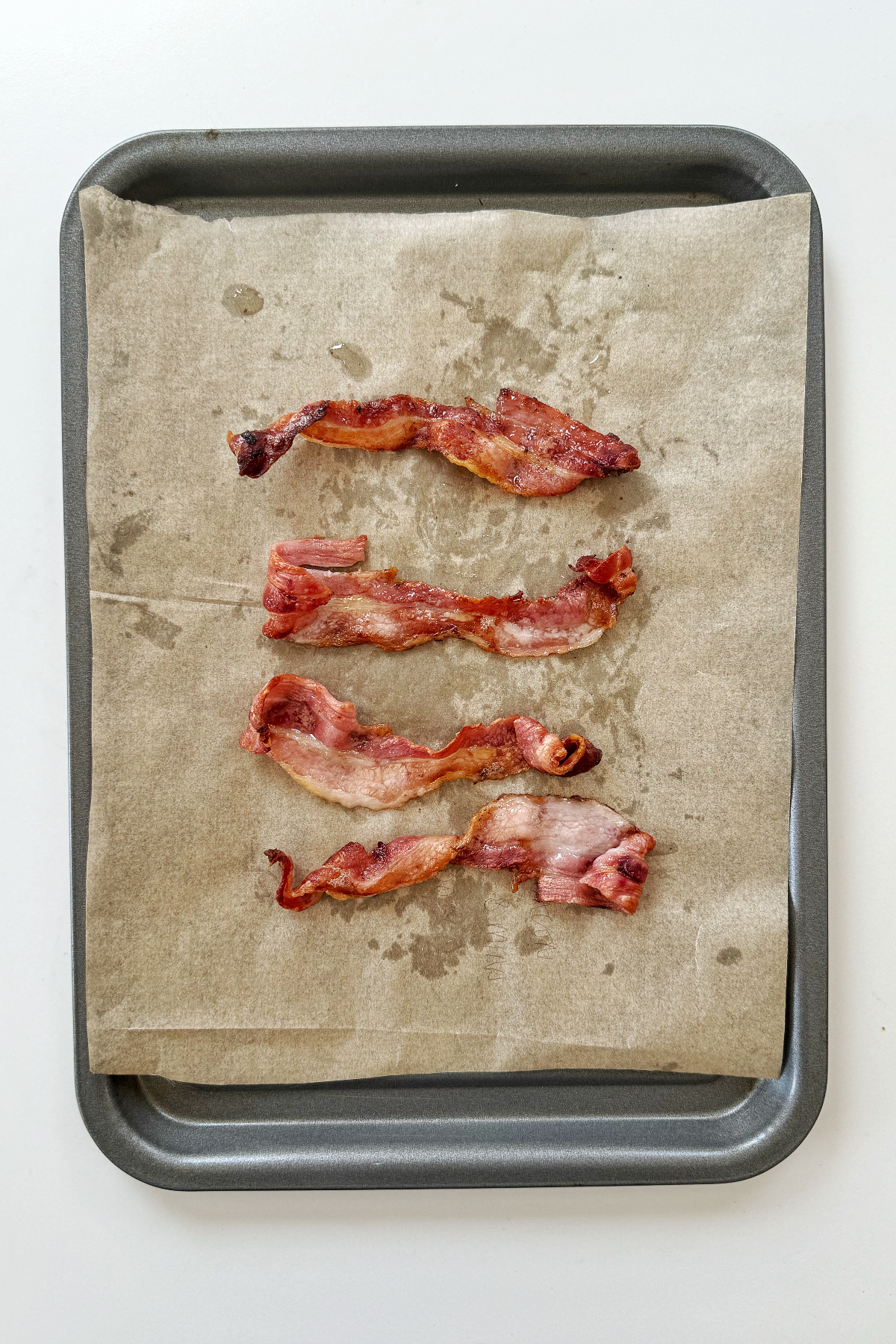 Less cooked streaky bacon on a tray.