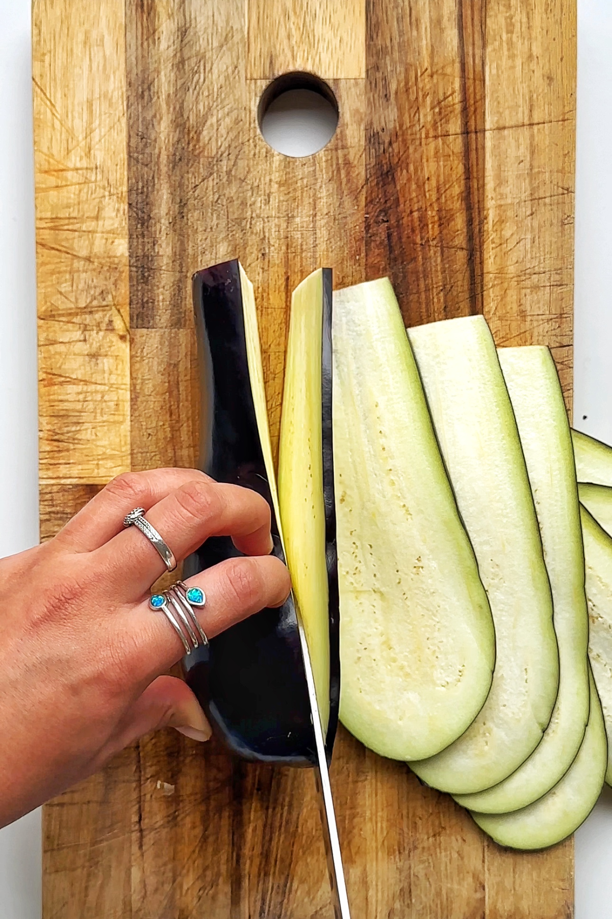Slicing eggplant on a wooden chopping board.