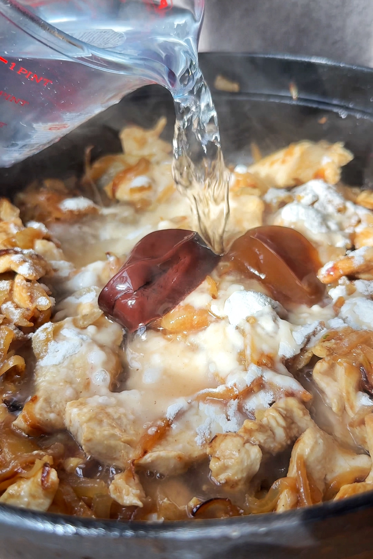 Pouring water into a chicken casserole French onion soup.