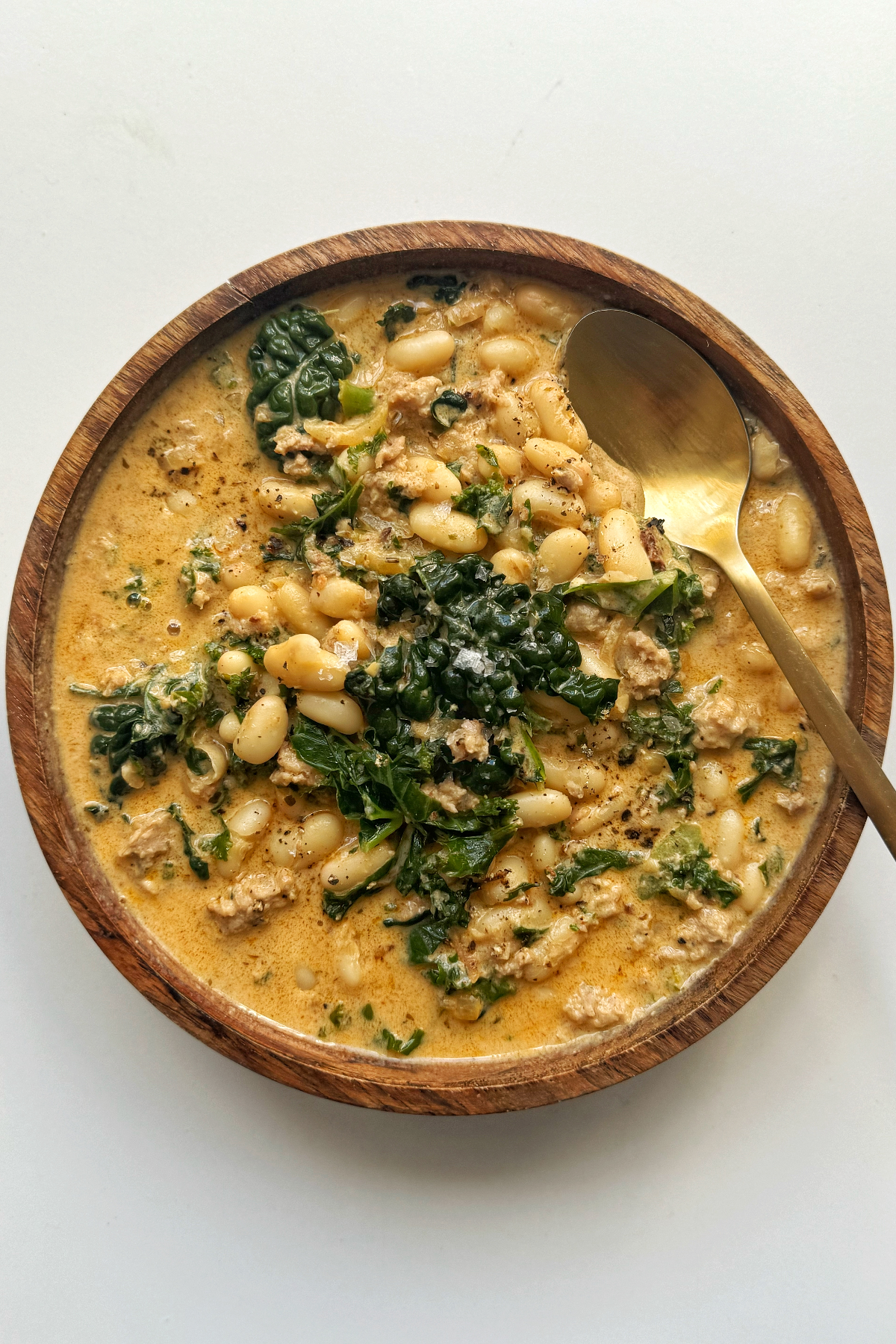 Kale and white bean sausage soup on white background.
