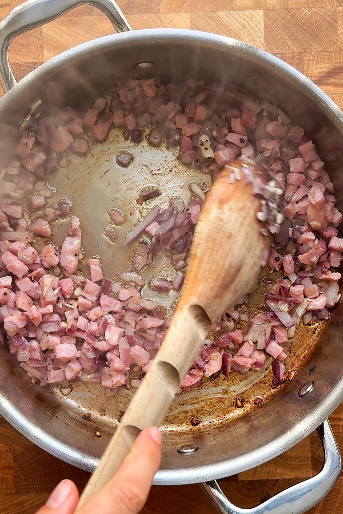 Frying garlic, onion, and lardons in a pan.