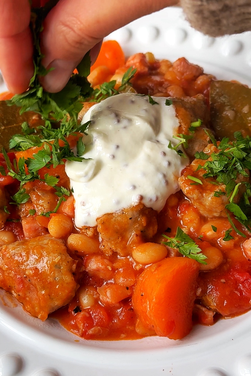 Topping the sausage stew with sour cream and wholegrain mustard and parsley.