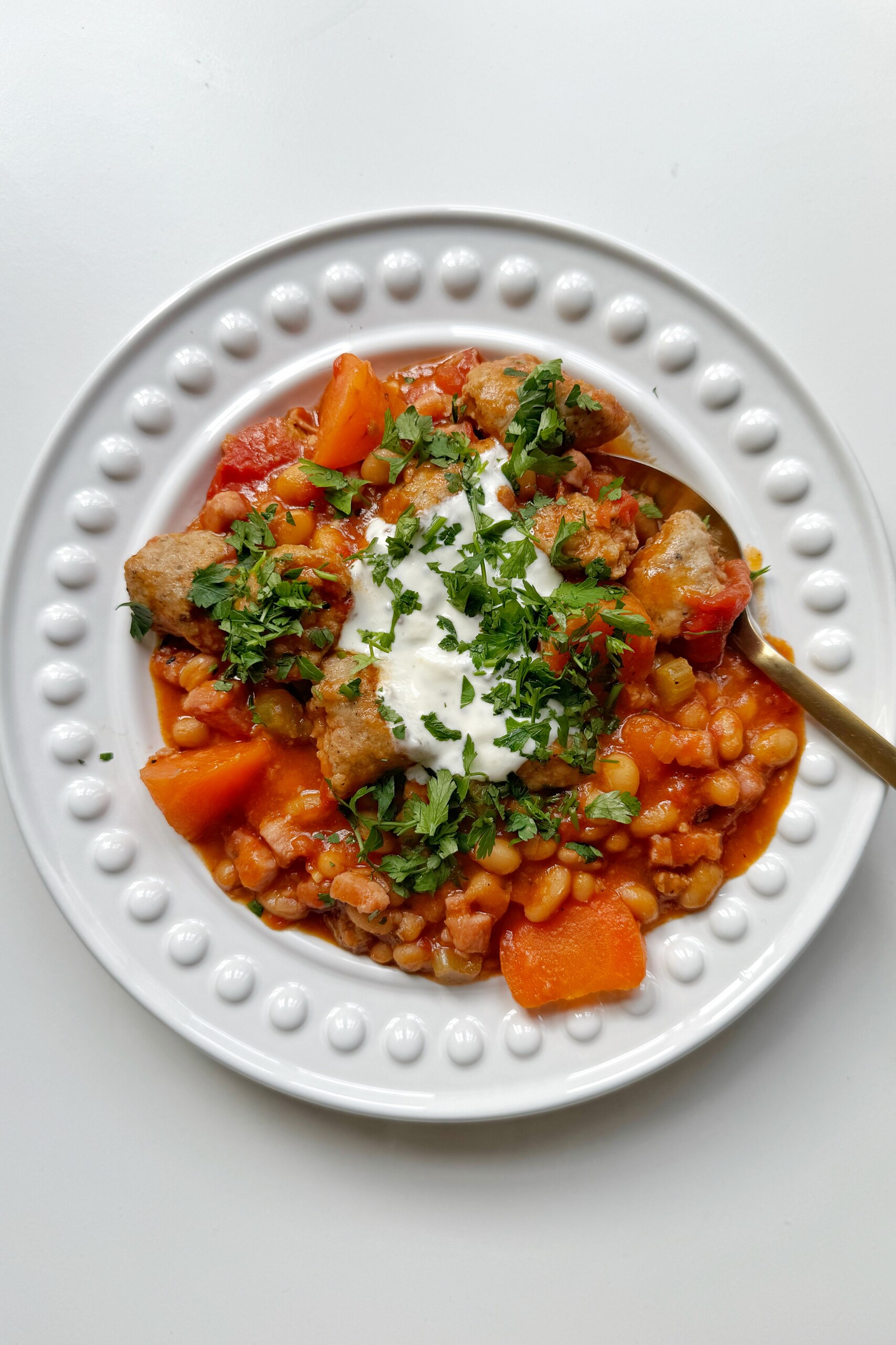 Sausage stew in a bowl topped with sour cream and parsley.