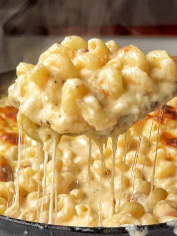 Black oven-proof dish filled with macaroni and cheese pull.