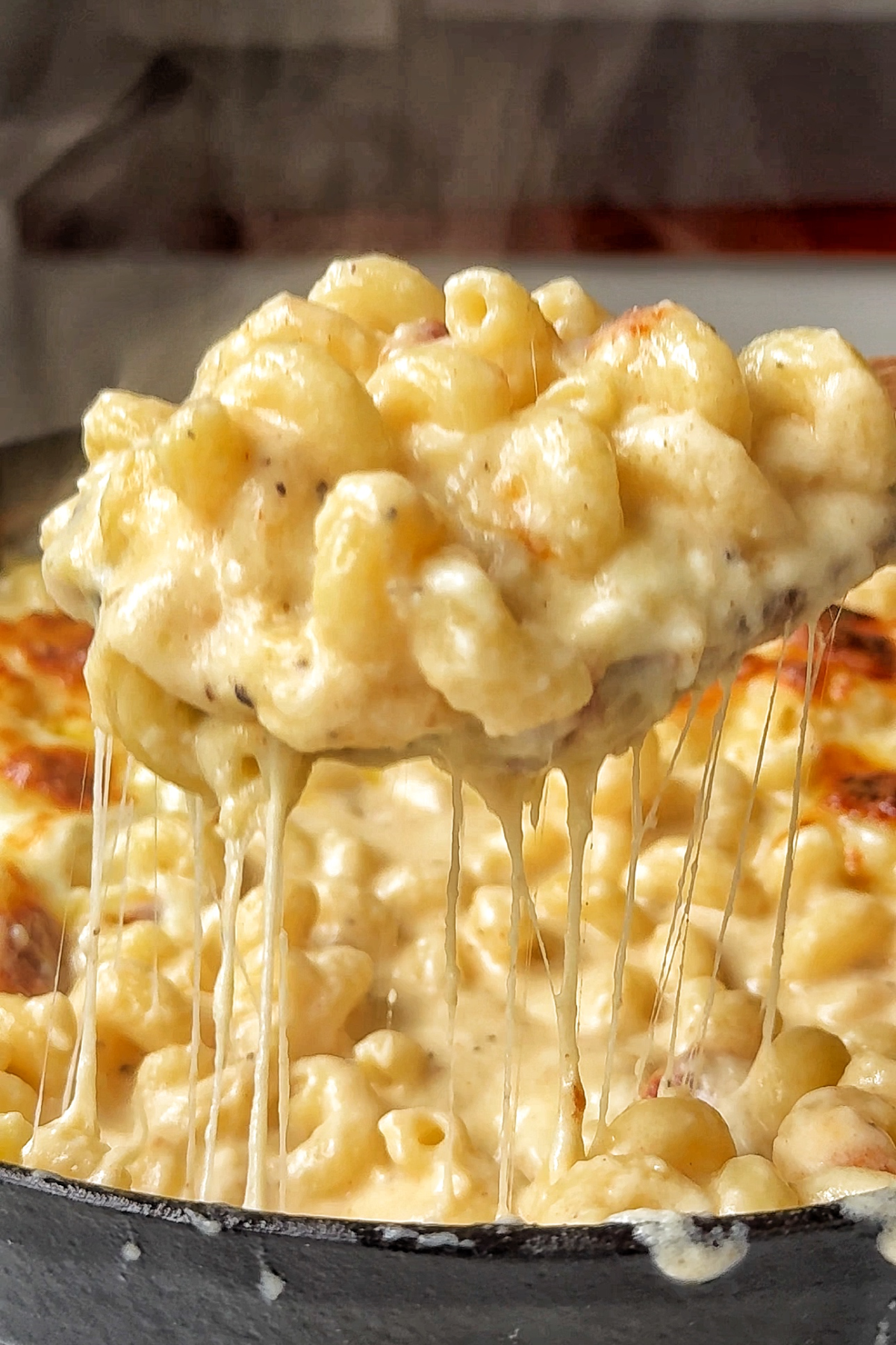 Black oven-proof dish filled with macaroni and cheese pull.