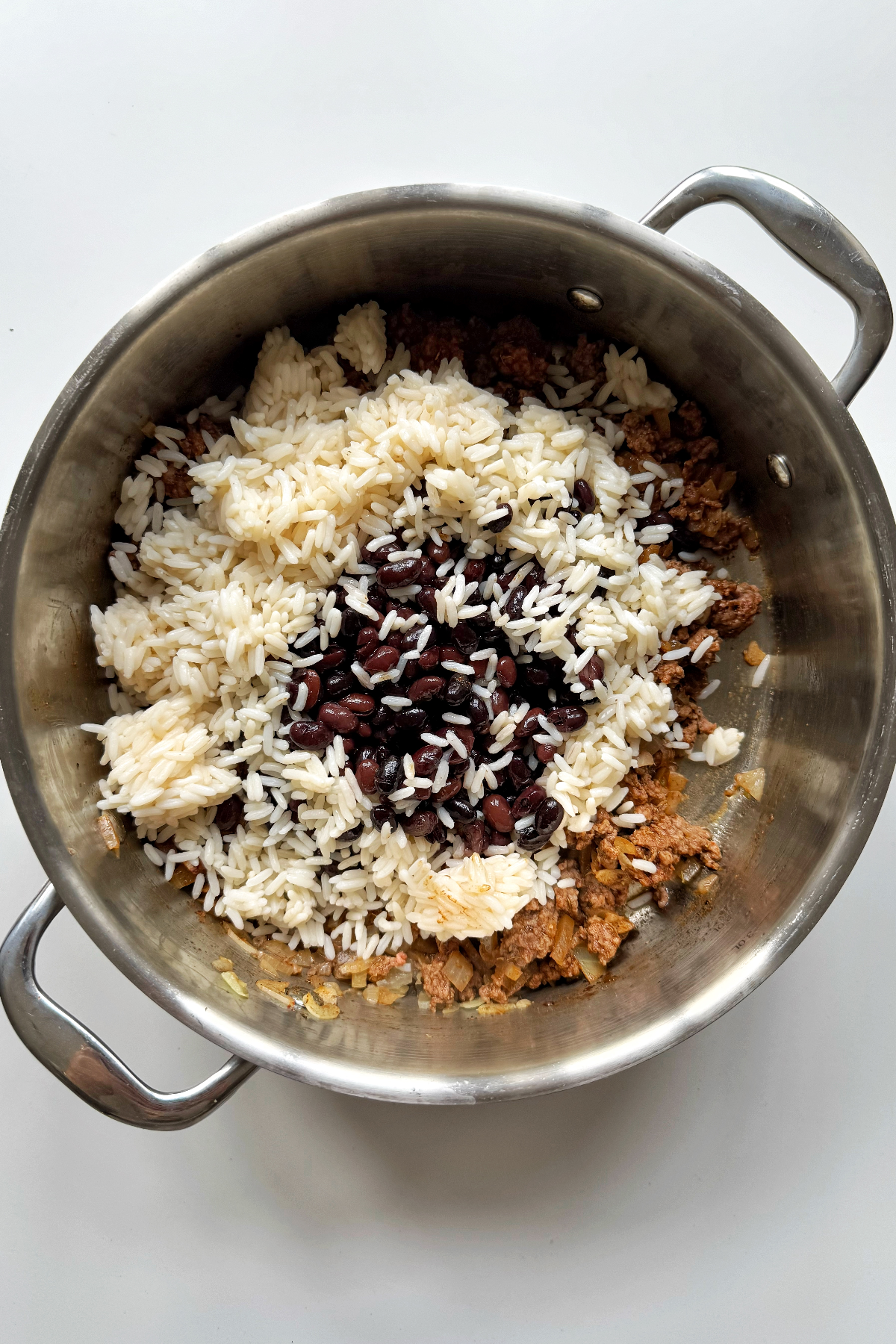 Adding rice and beans to the ground beef stuffed pepper mixture.