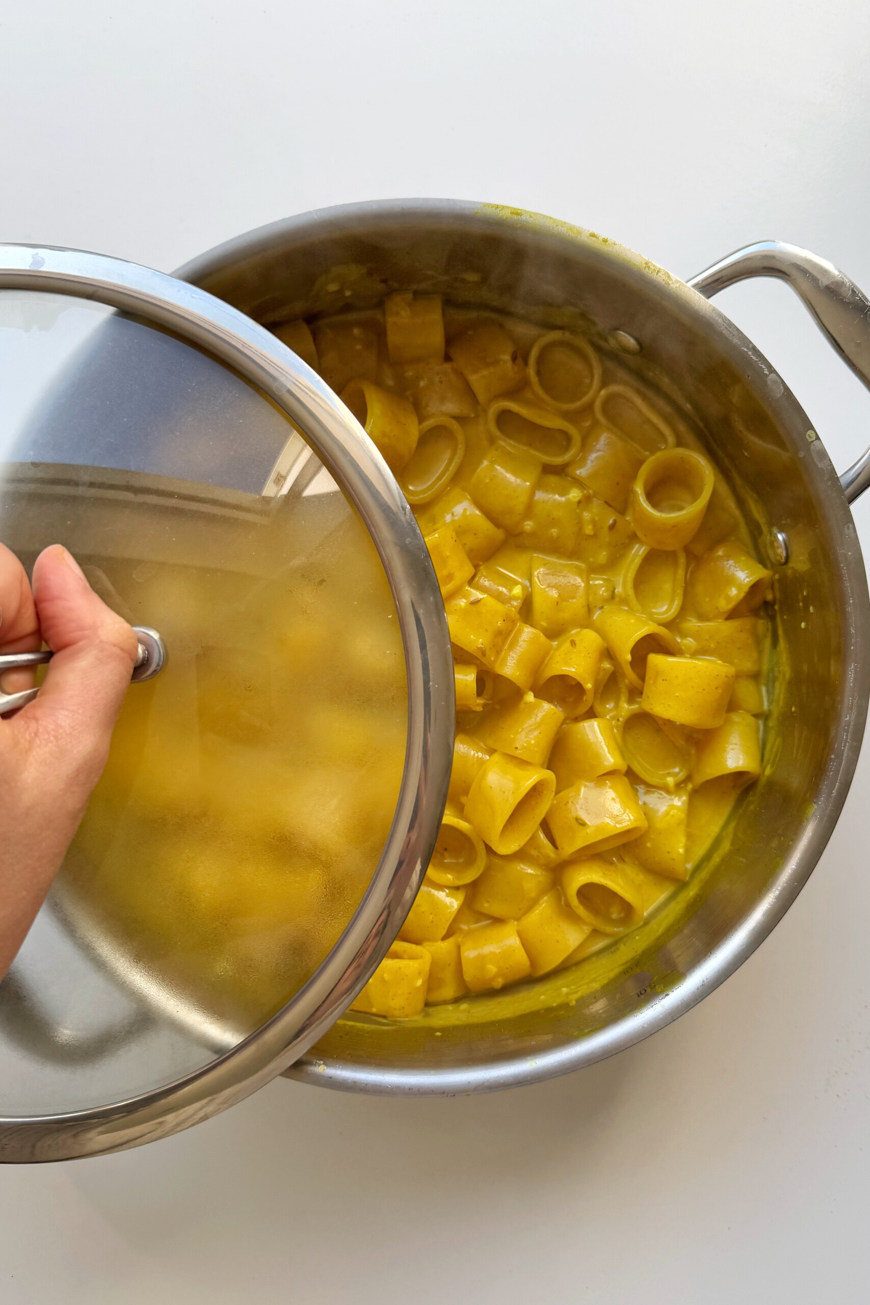 Cooking curry pasta with lid of metal pan.