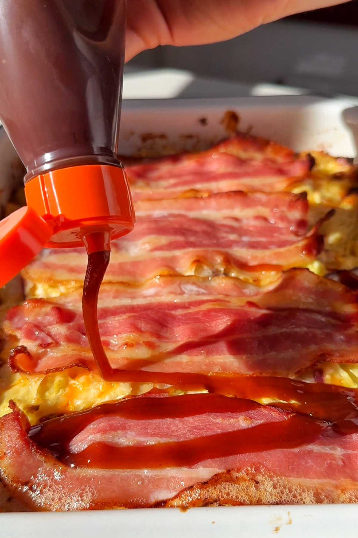 Drizzling brown sauce over the cooked okonomiyaki traybake.