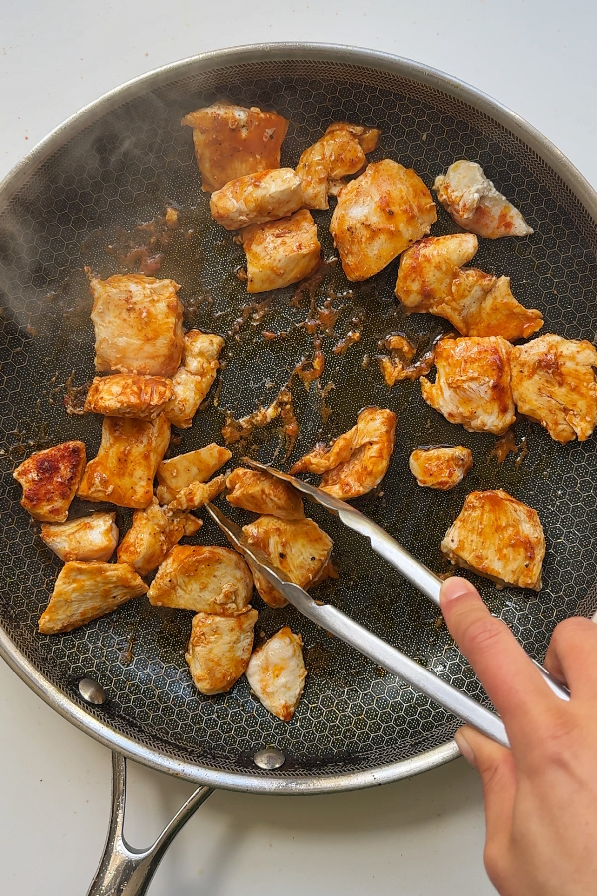 Cooking chicken in black frying pan.