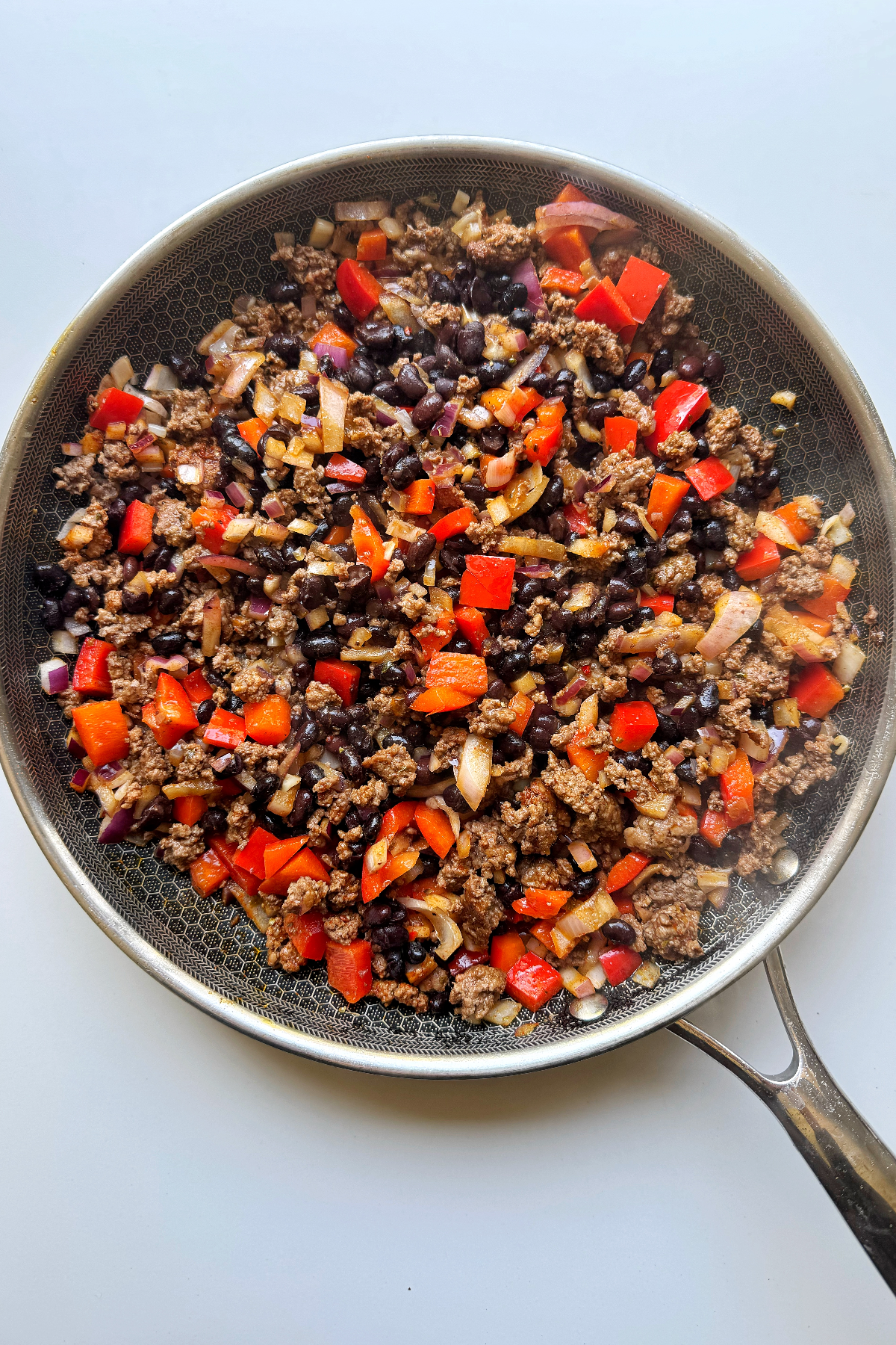 Frying ground beef in pan with red peppers onion and spices.