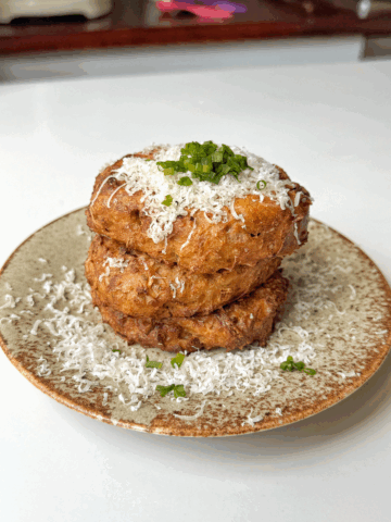 Air fryer hash browns stacked on a plate topped with parmesan and chives.