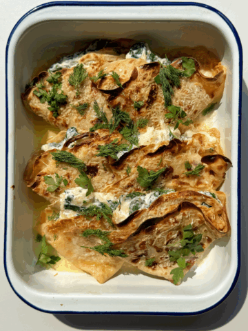 Crespelle in baking dish topped with dill and parsley.