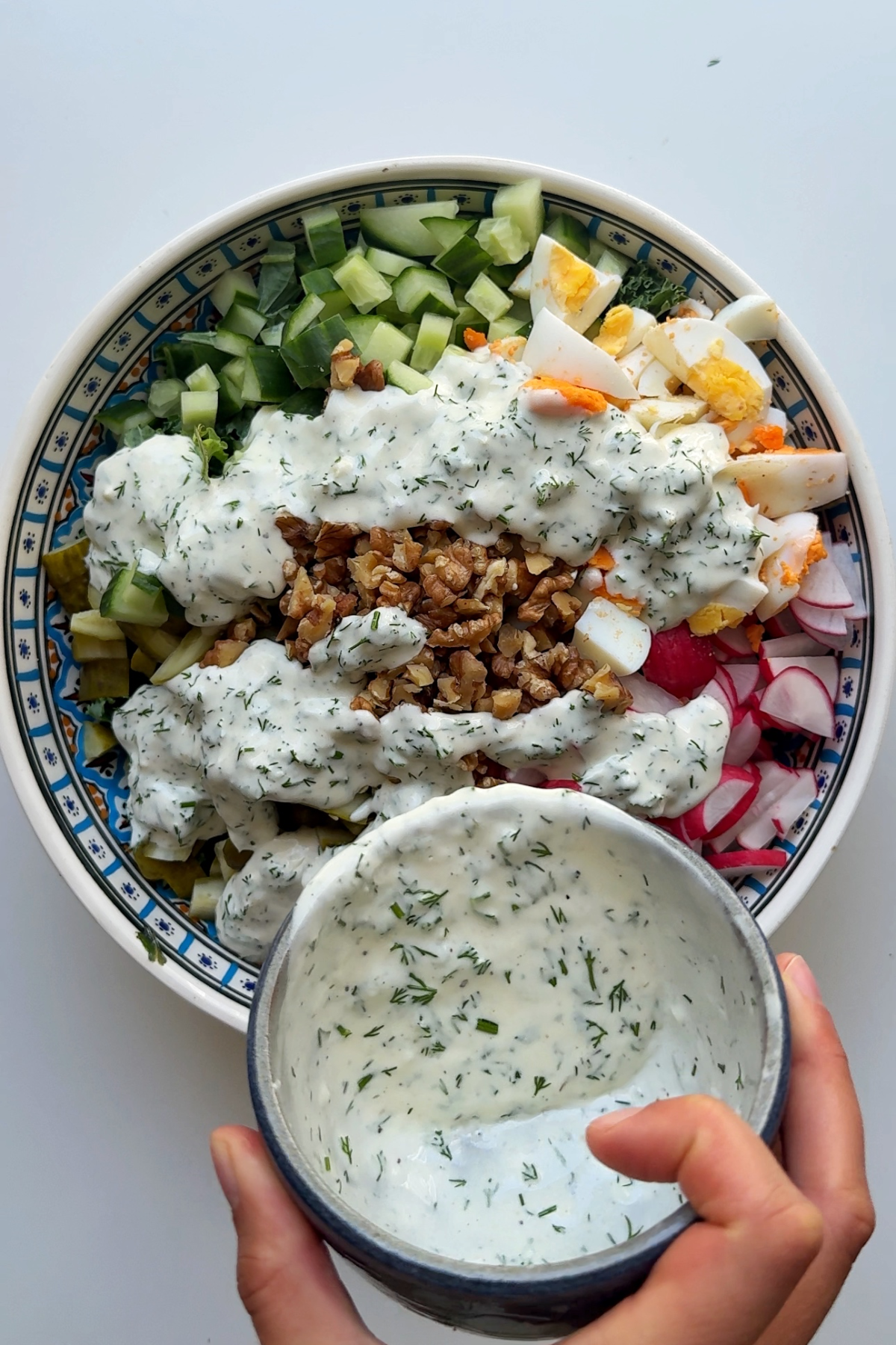 Pouring salad dressing over chopped salad in bowl.