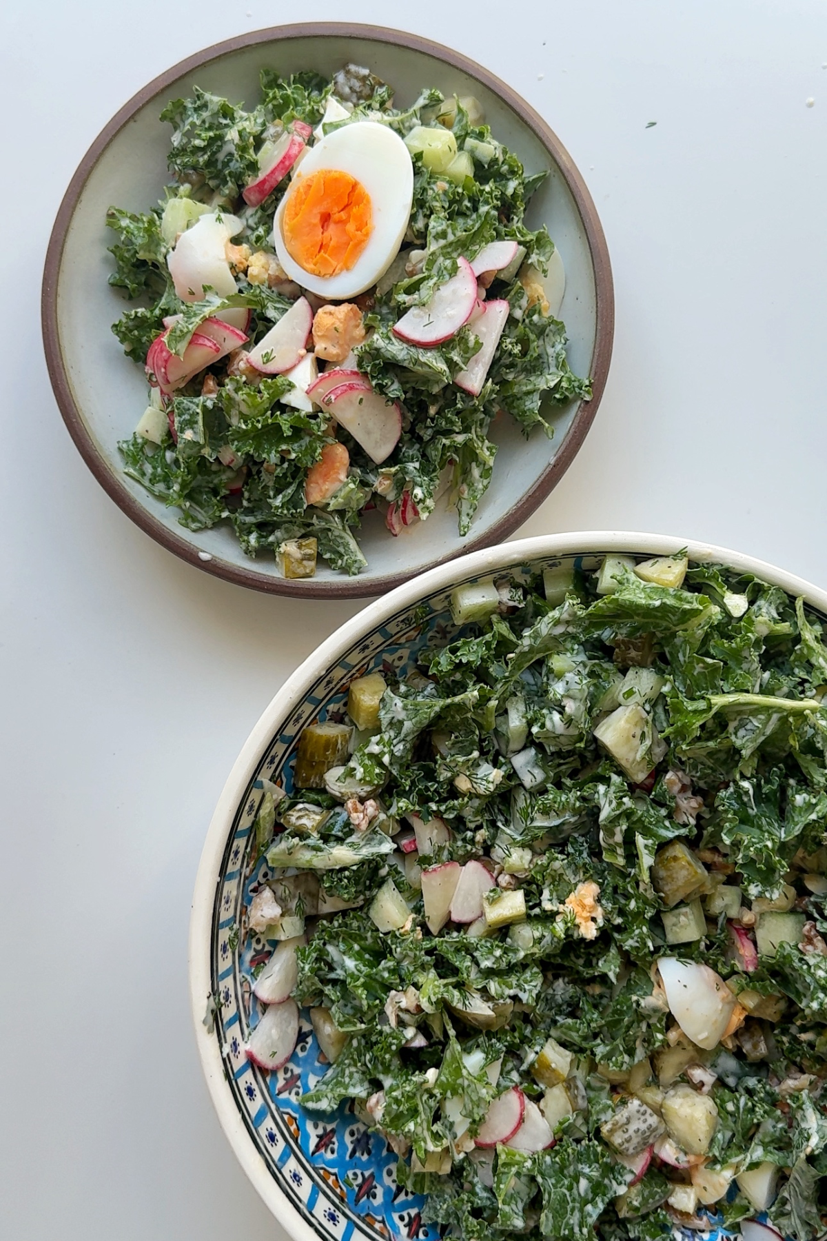 Dill pickle egg salad in bowl and in serving bowl with boiled egg on top.