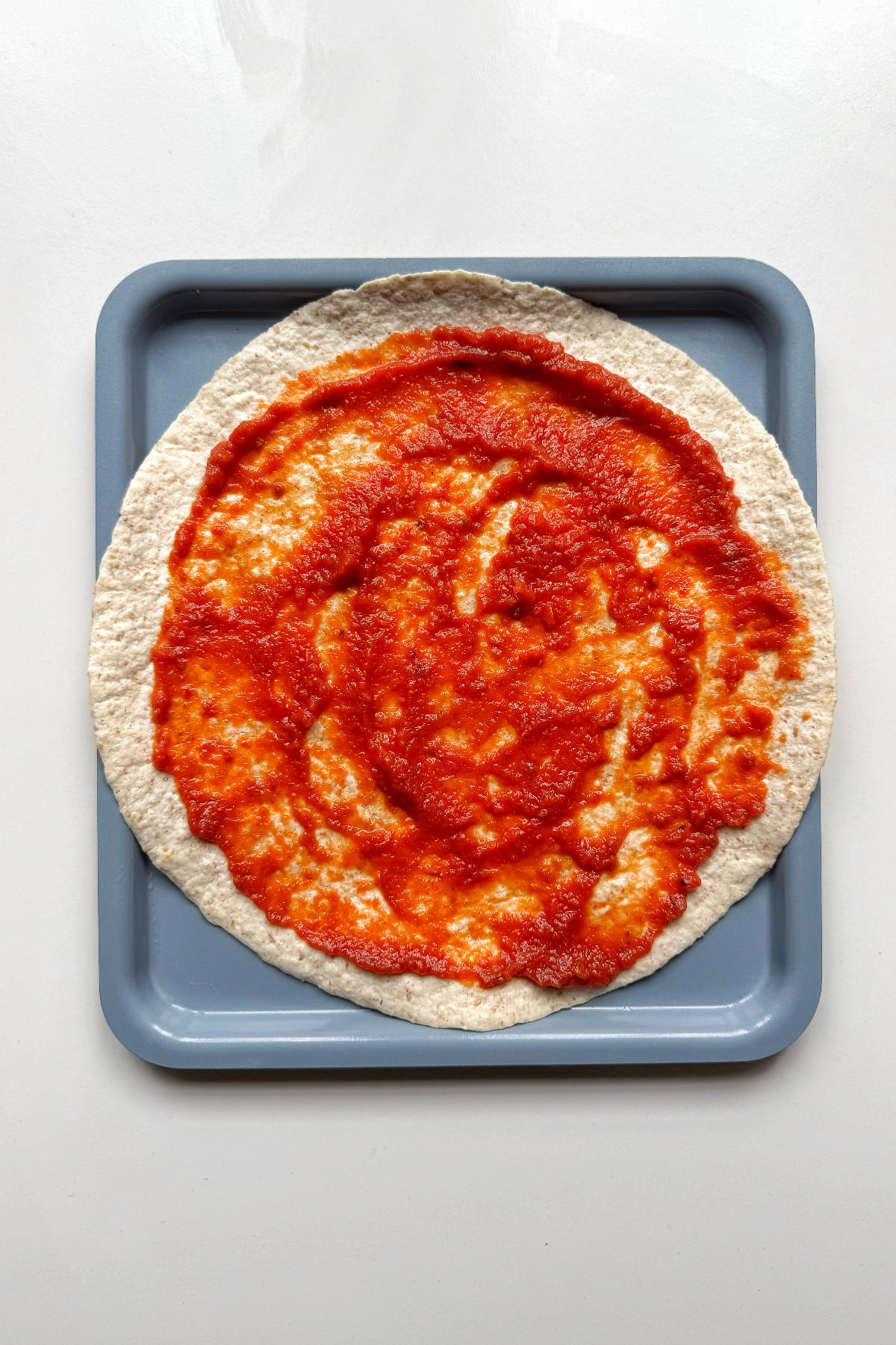 Topping the pizza wrap with marinara sauce.