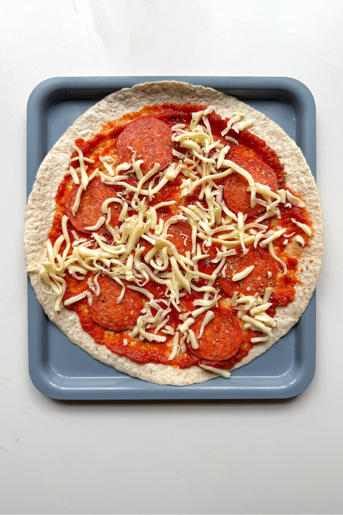 Top the pizza wrap with pepperoni and mozzarella cheese on a blue tray.