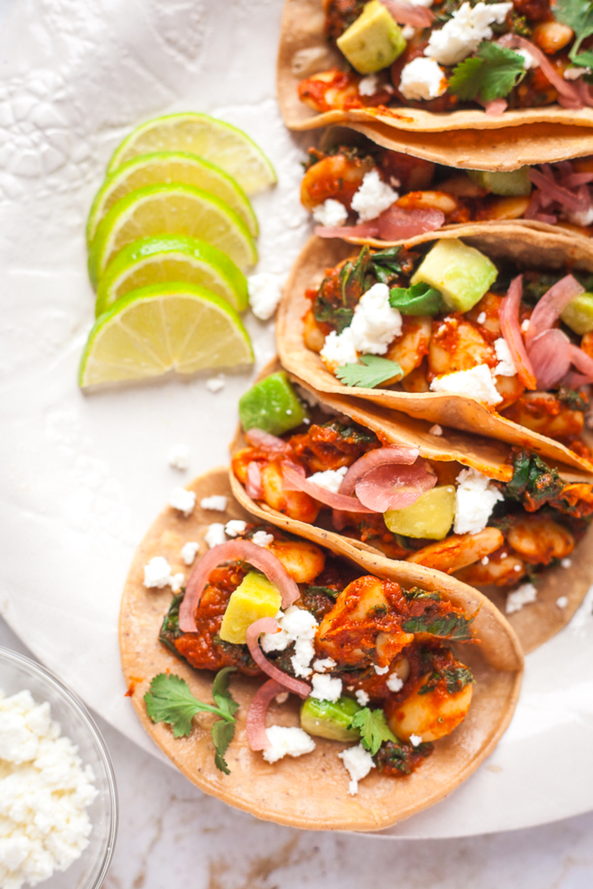 Butter bean tacos on a white plate with lime wedges and cilantro