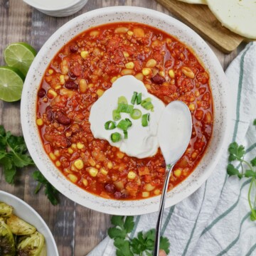 A bowl of sweet corn, bean and beef chili, with a dollop of sour cream on top and sprinkled chives.