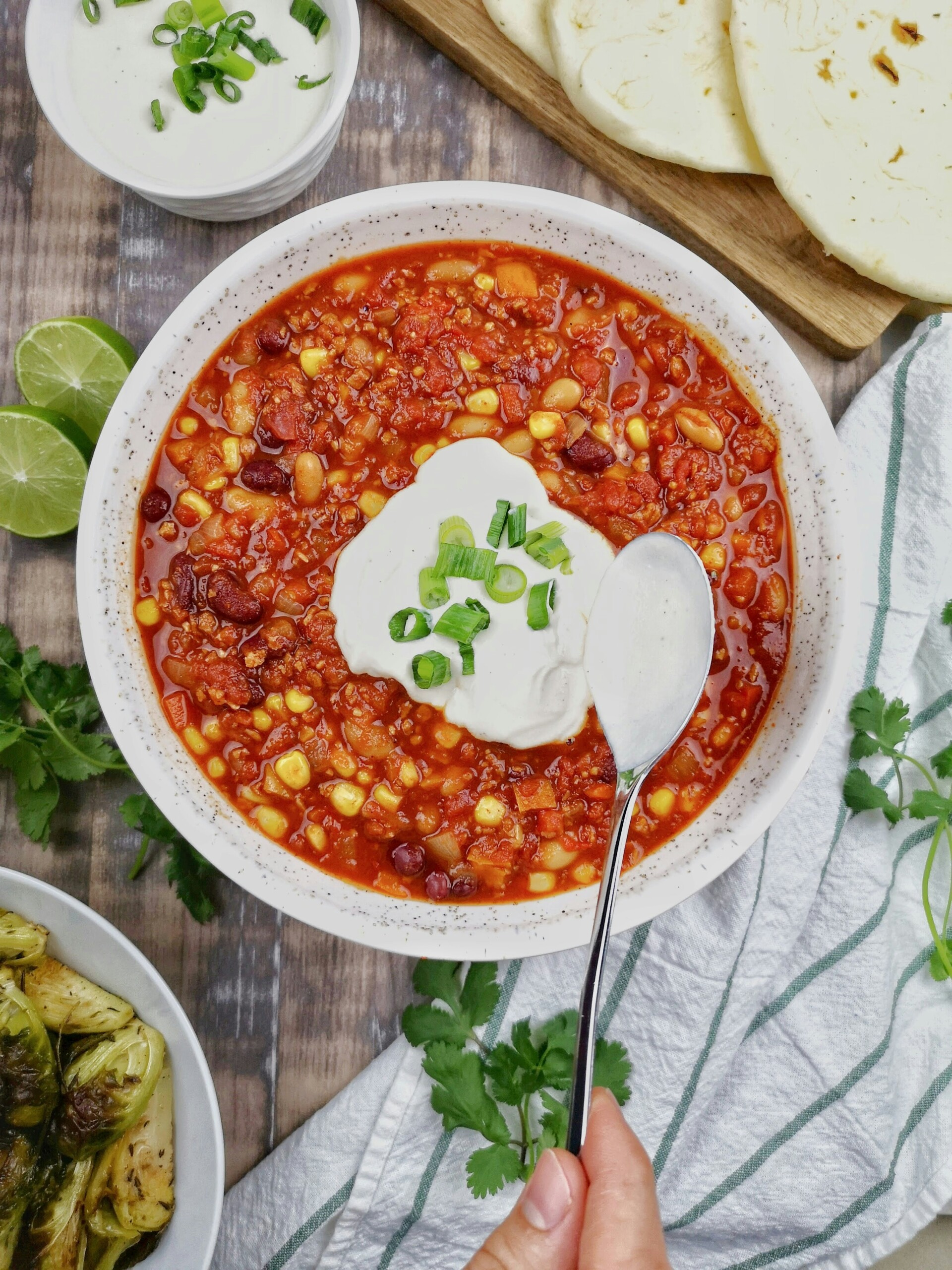 A bowl of sweet corn, bean and beef chili, with a dollop of sour cream on top and sprinkled chives.