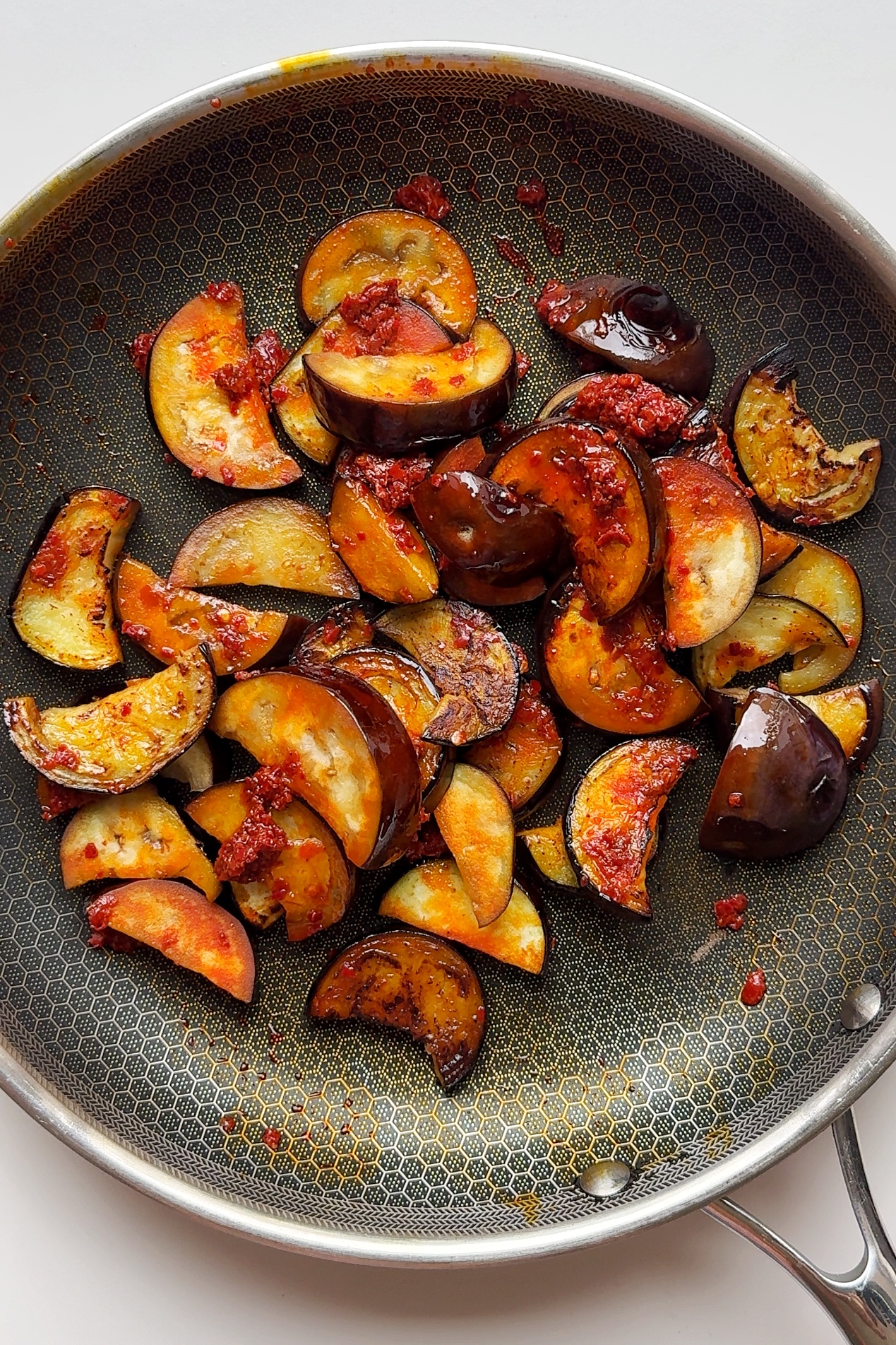 Frying aubergine with harissa in pan.