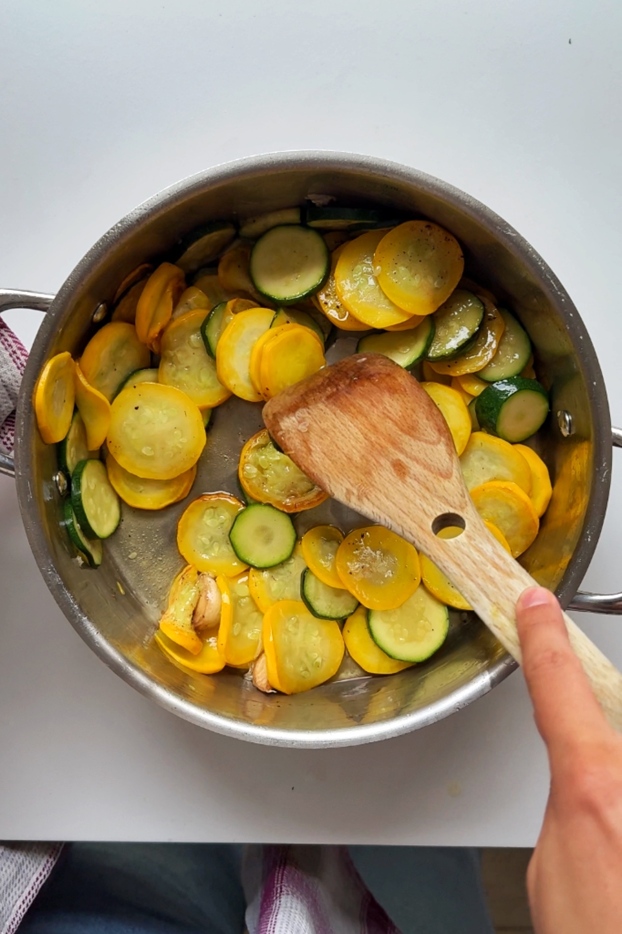 Frying courgette in a pan with olive oil and whole garlic cloves.