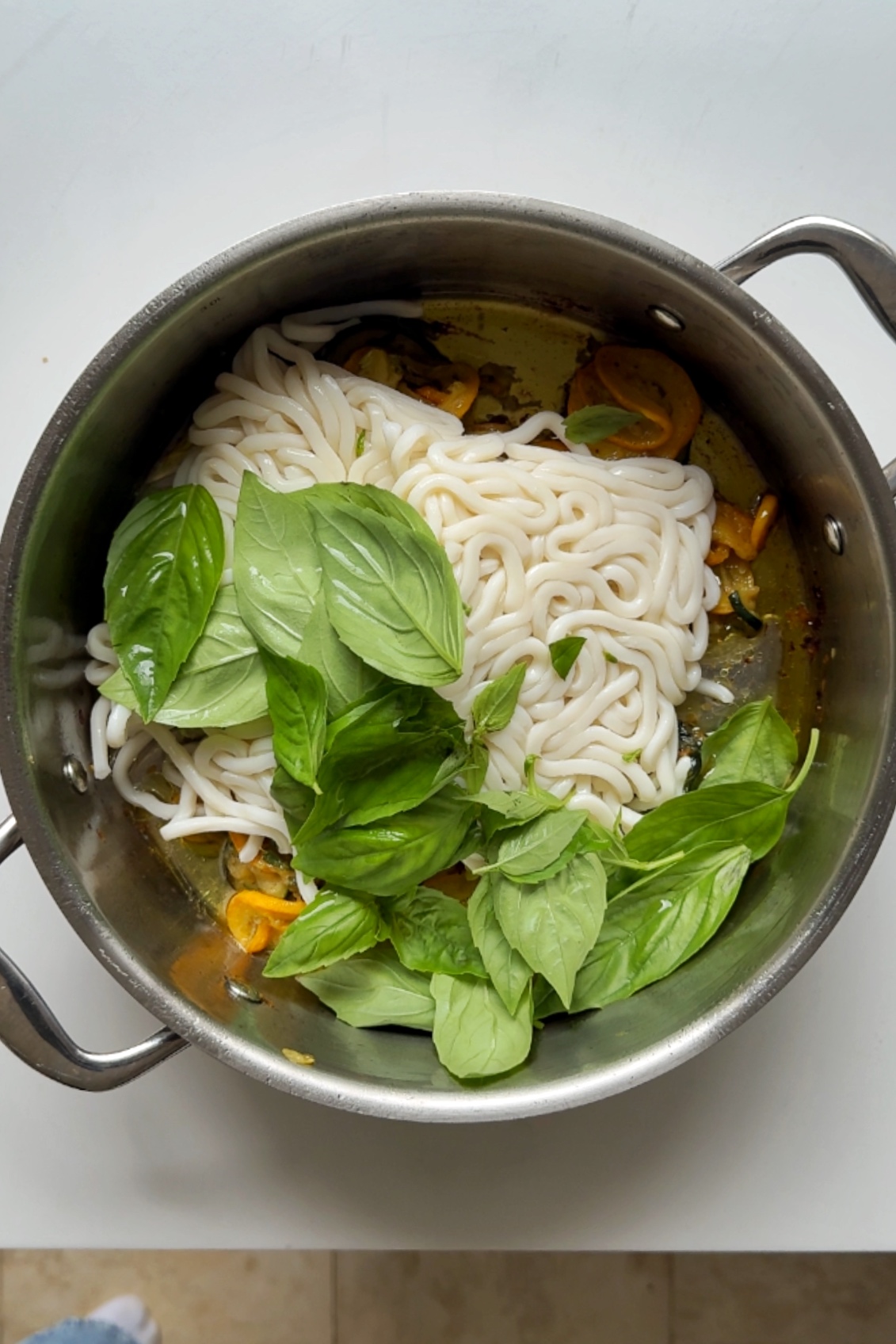 Adding noodles and basil to courgette pan.