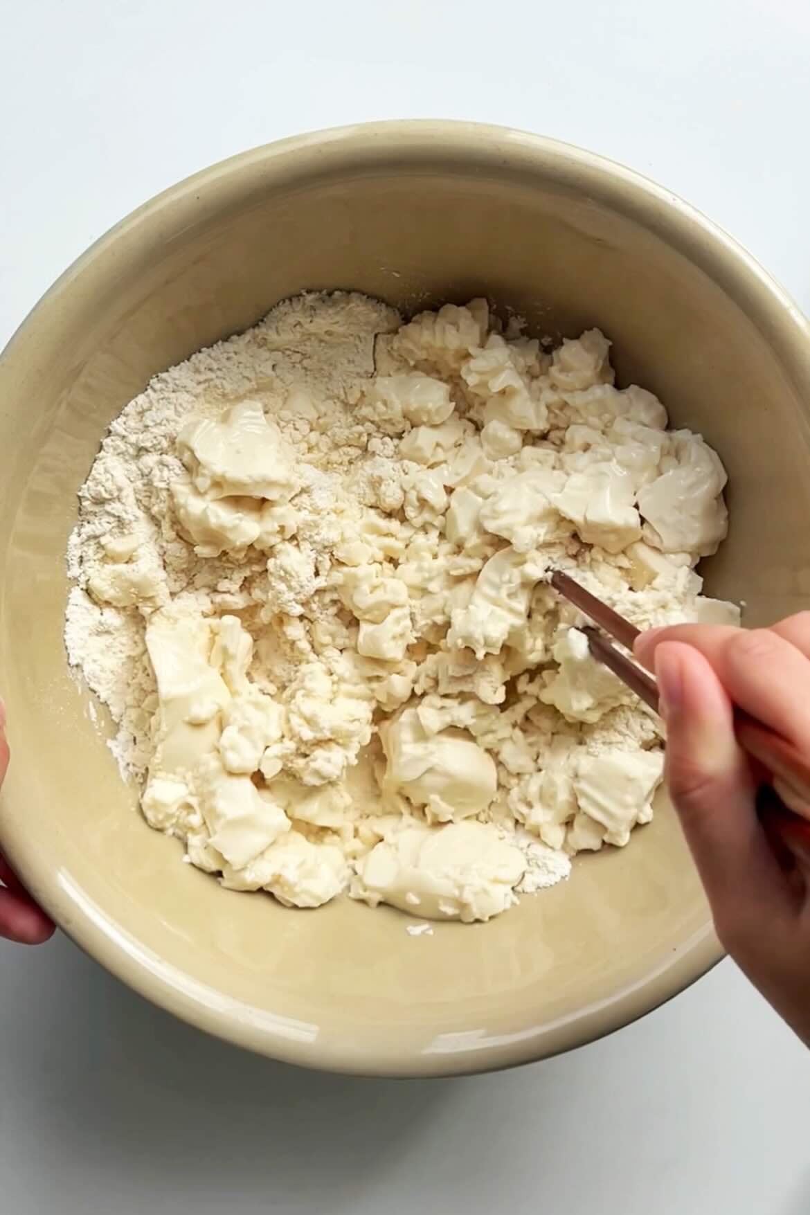 A bowl of silken tofu being blended with pair of chopsticks.