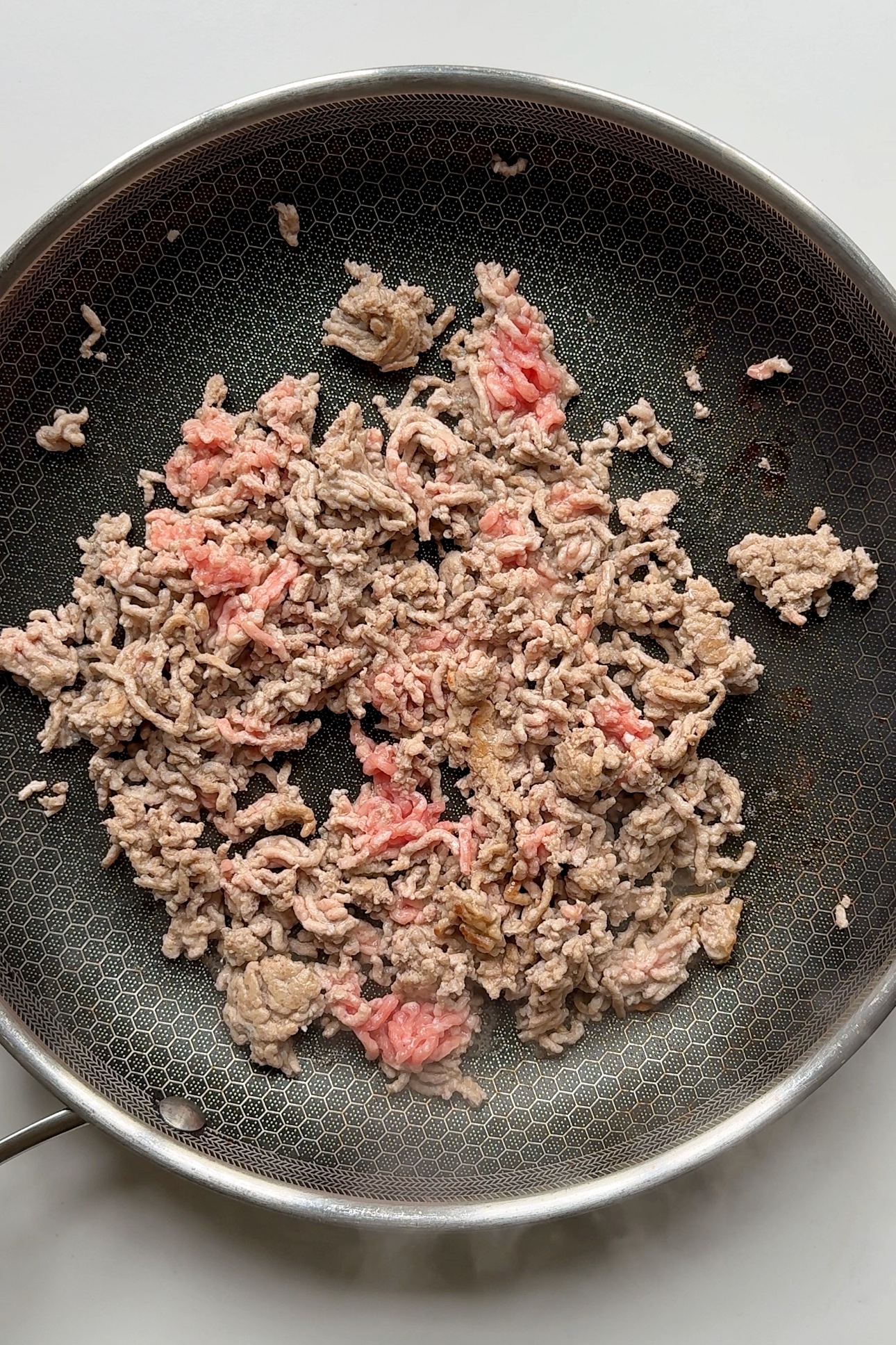 Frying ground pork in black pan.