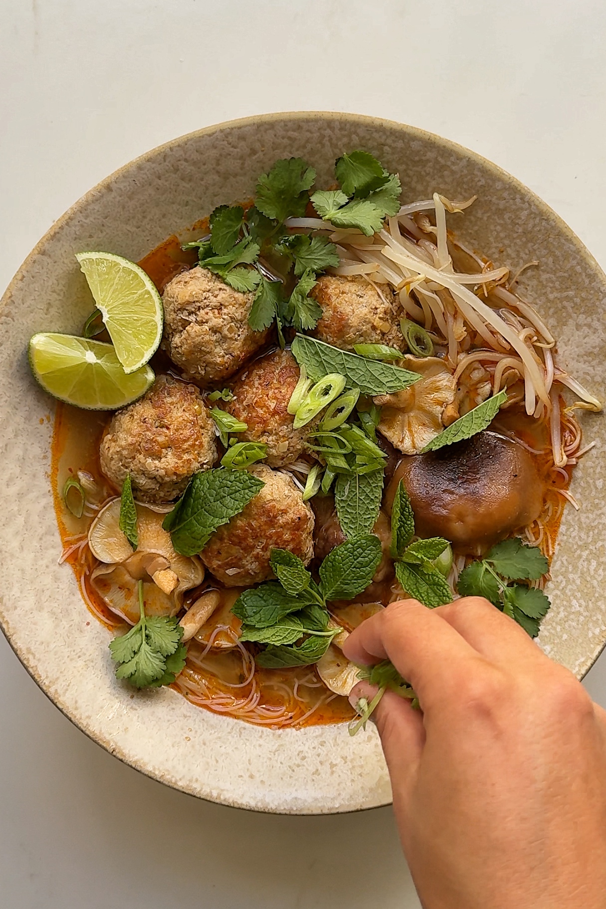 sprinkling herbs onto pork meatball soup.