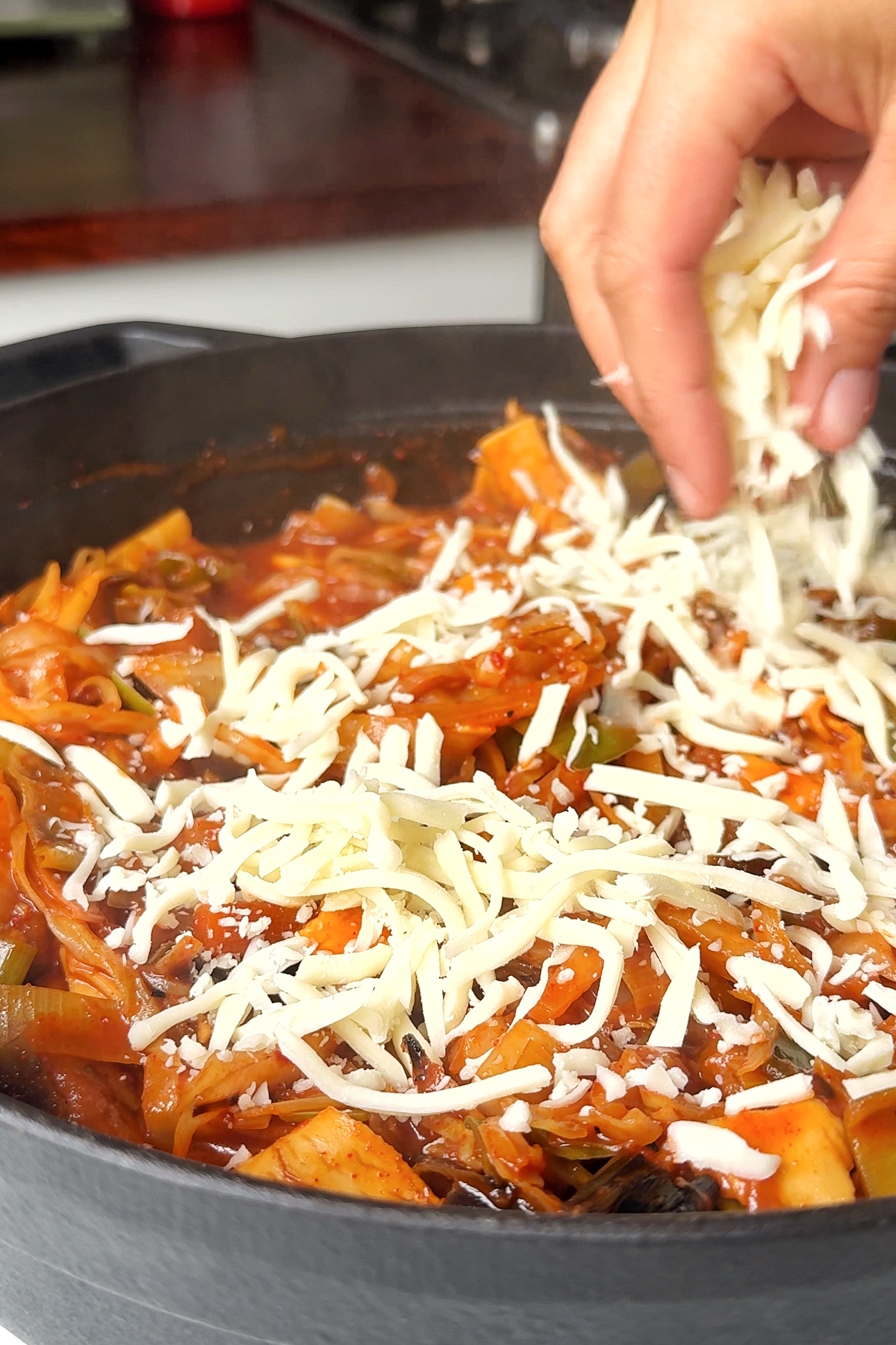 adding grated cheese to spicy gochujang lasagne.