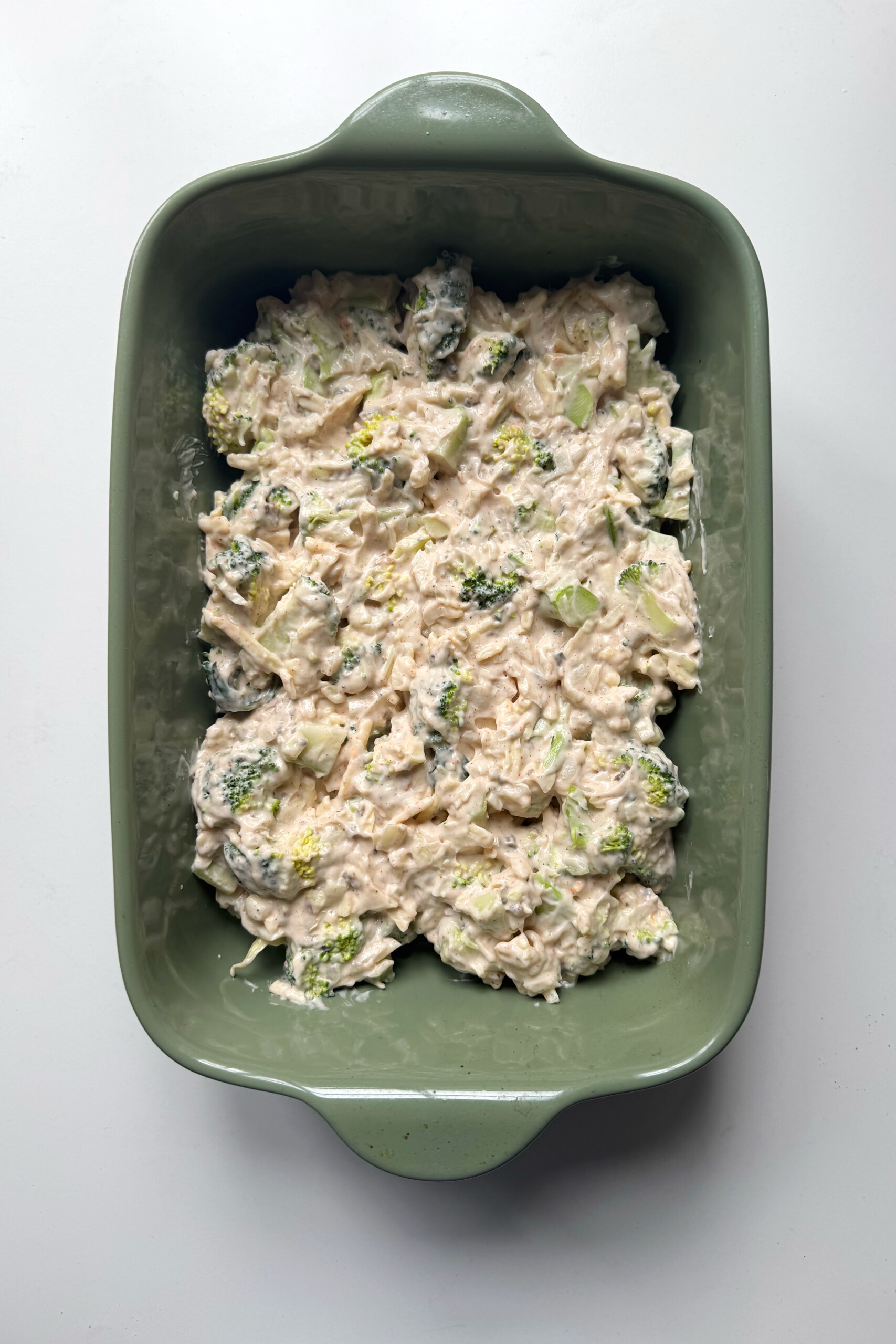 green dish with broccoli casserole and cheddar cheese.