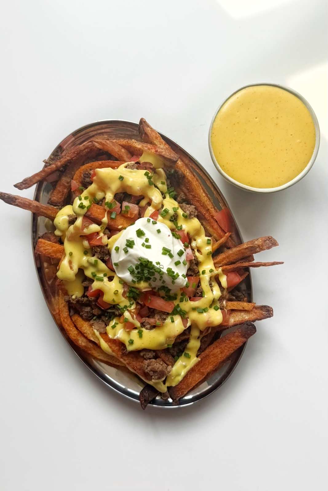 Loaded nacho fries topped with ground beef, cheese sauce, tomatoes, sour cream and chives on an oval platter