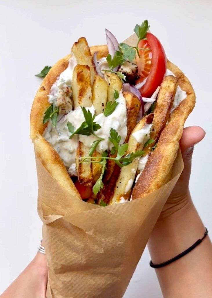 A hand-held chicken gyro wrap filled with air-fried potato fries, fresh tomatoes, red onion, and tzatziki sauce.