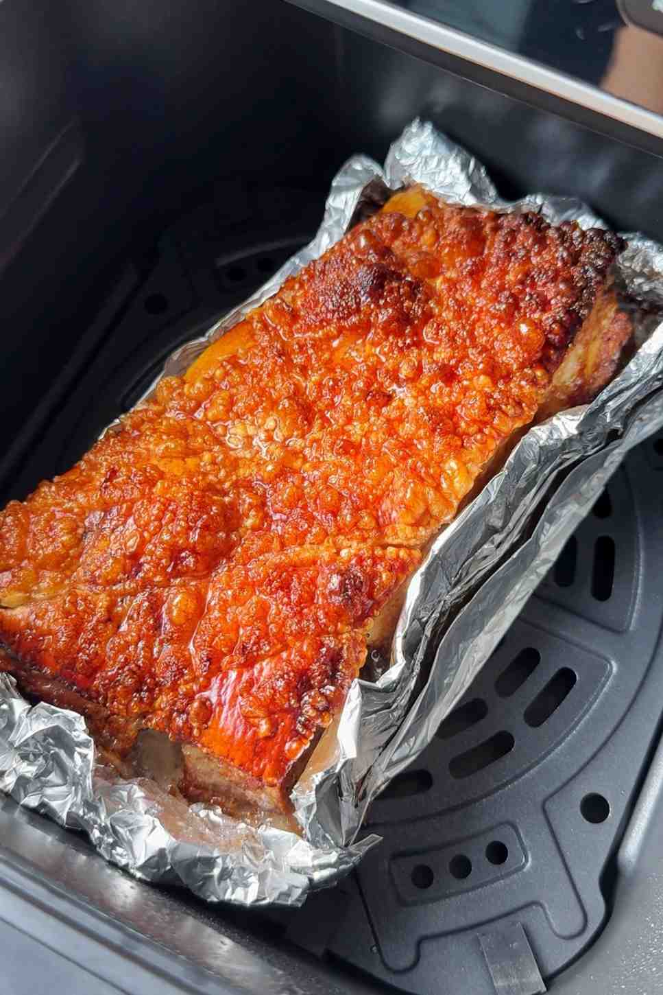 High-angle shot of pork belly in an ninja air fryer basket with perfectly bubbled, golden-brown crispy crackling.