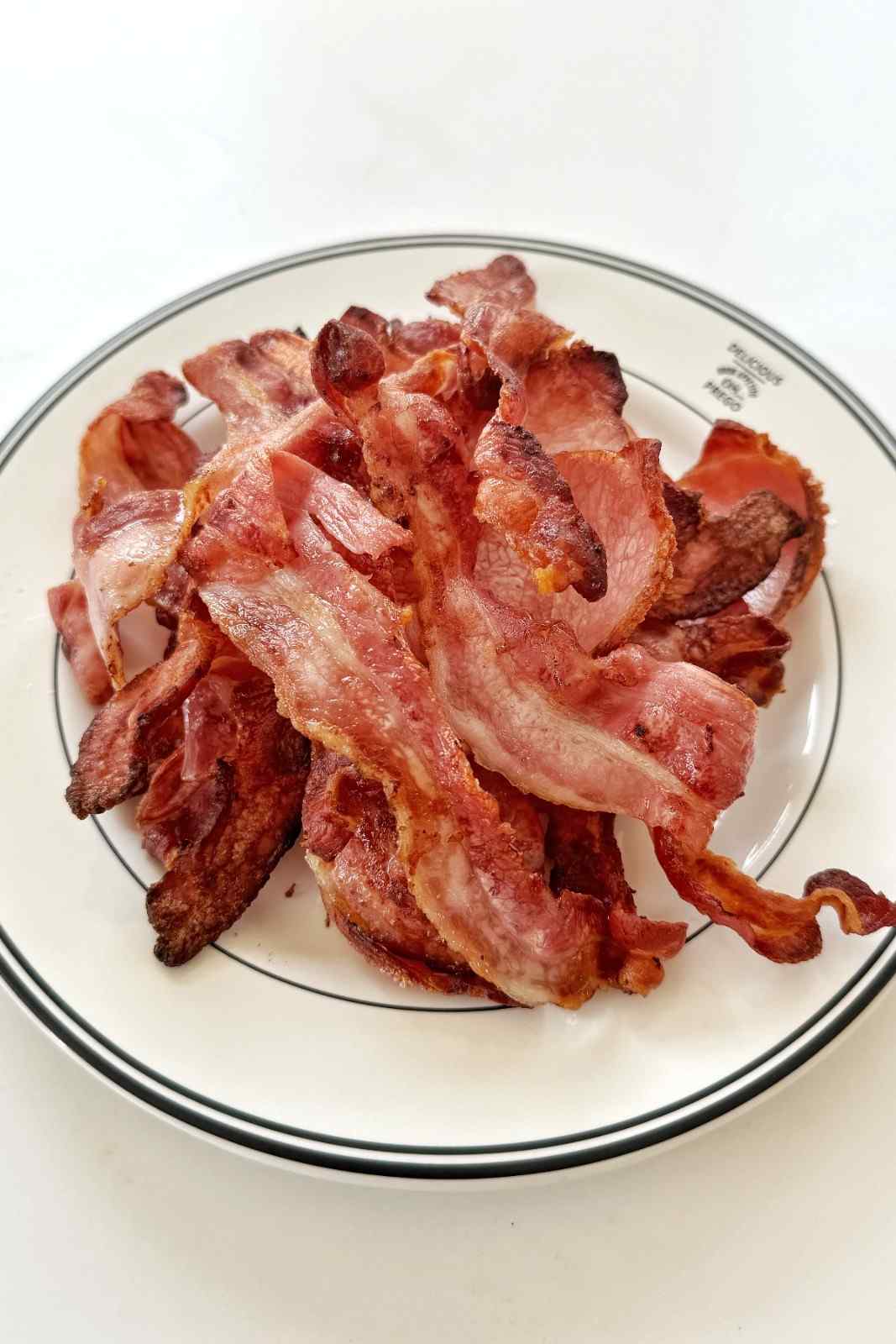 A plate of perfectly crisped, wavy bacon strips cooked to a deep golden brown in a ninja air fryer.