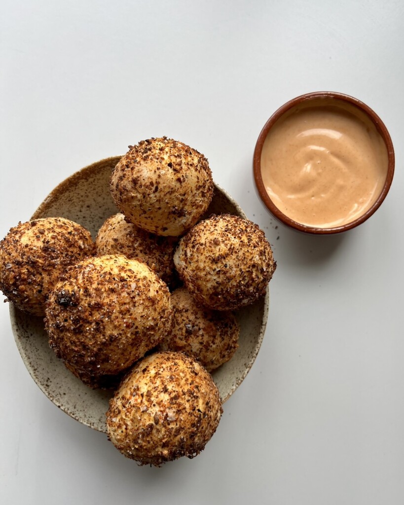 A bowl of golden-brown air-fried bread bites coated in a peppery herb seasoning, served with a small dish of creamy dipping sauce.