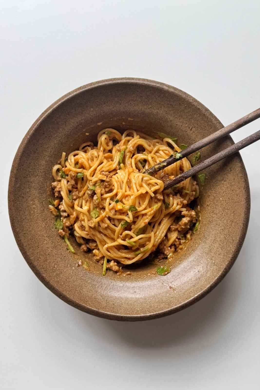 brown bowl with chopsticks filled with Thai-style peanut butter noodles