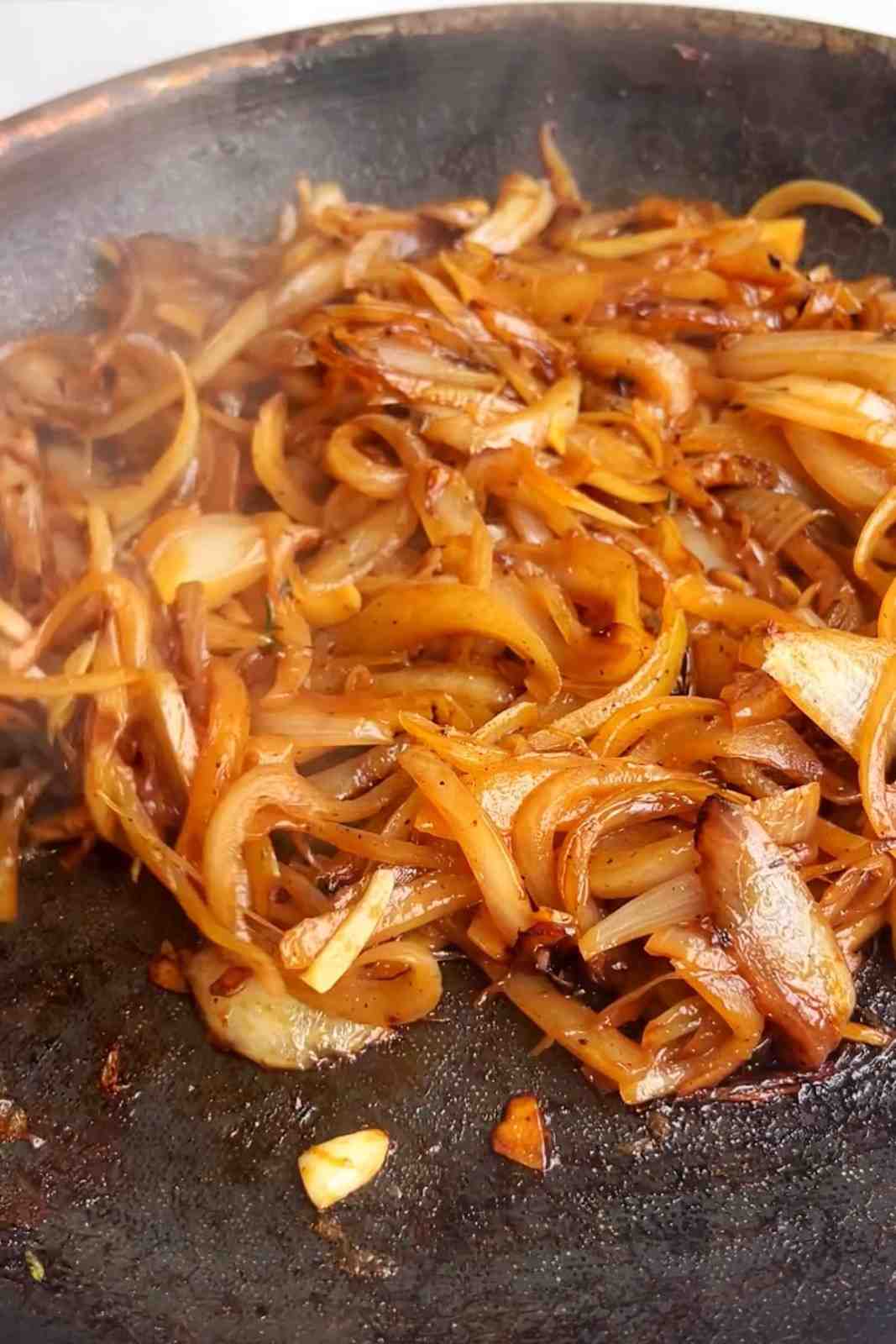 Deeply golden caramelized onions cooked down in a dark cast iron skillet until jammy and sticky.