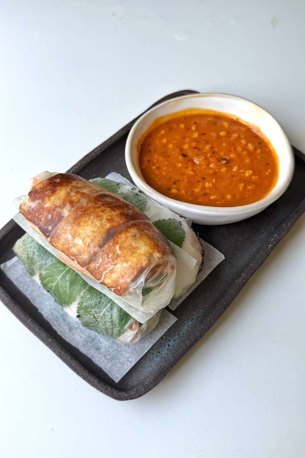 summer rolls stacked on a plate with a pot of peanut dipping sauce.